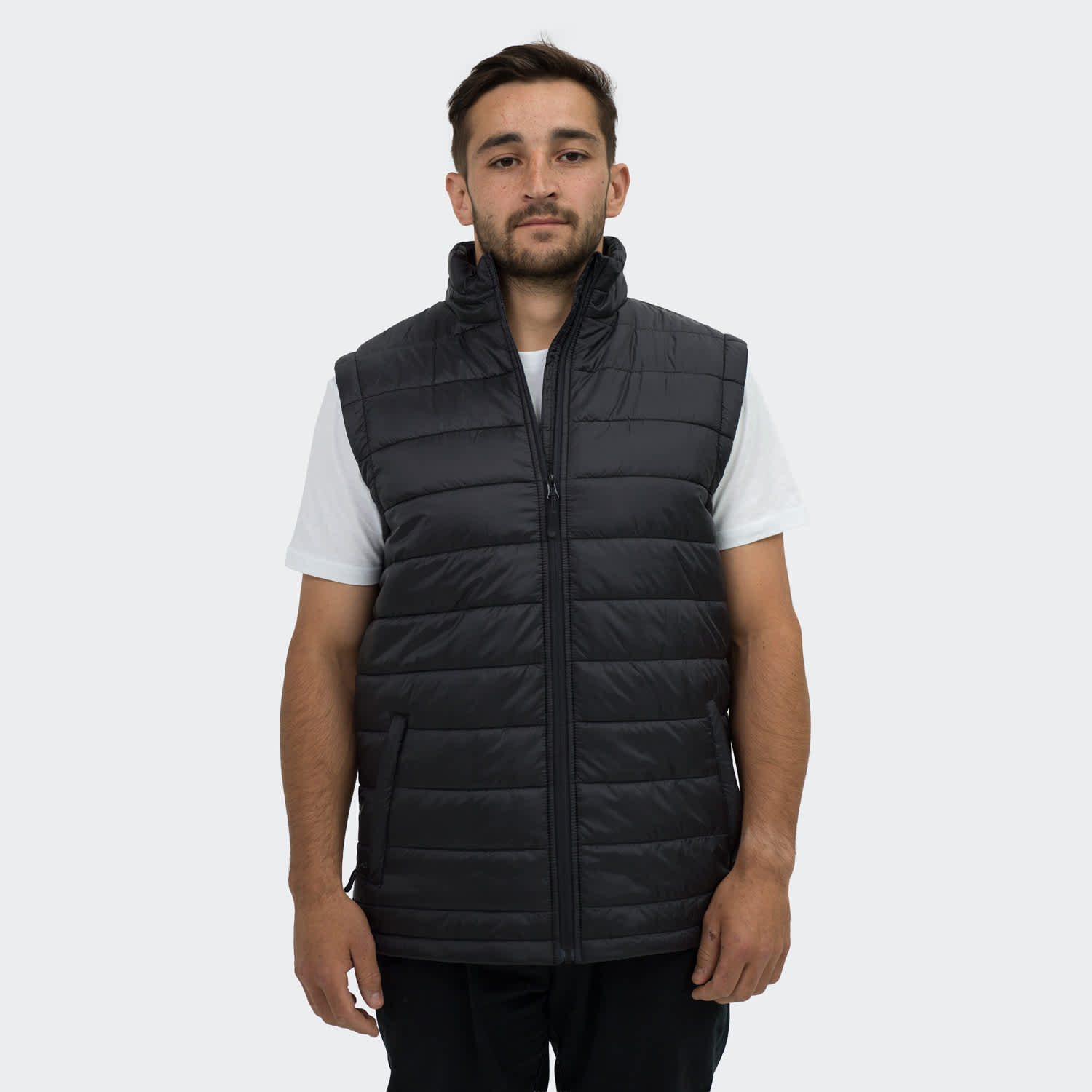 A man wearing a black puffer vest with a high collar and zippered front, featuring side pockets. TRENDSWEAR Payton Unisex Puffer Vest - Image 1