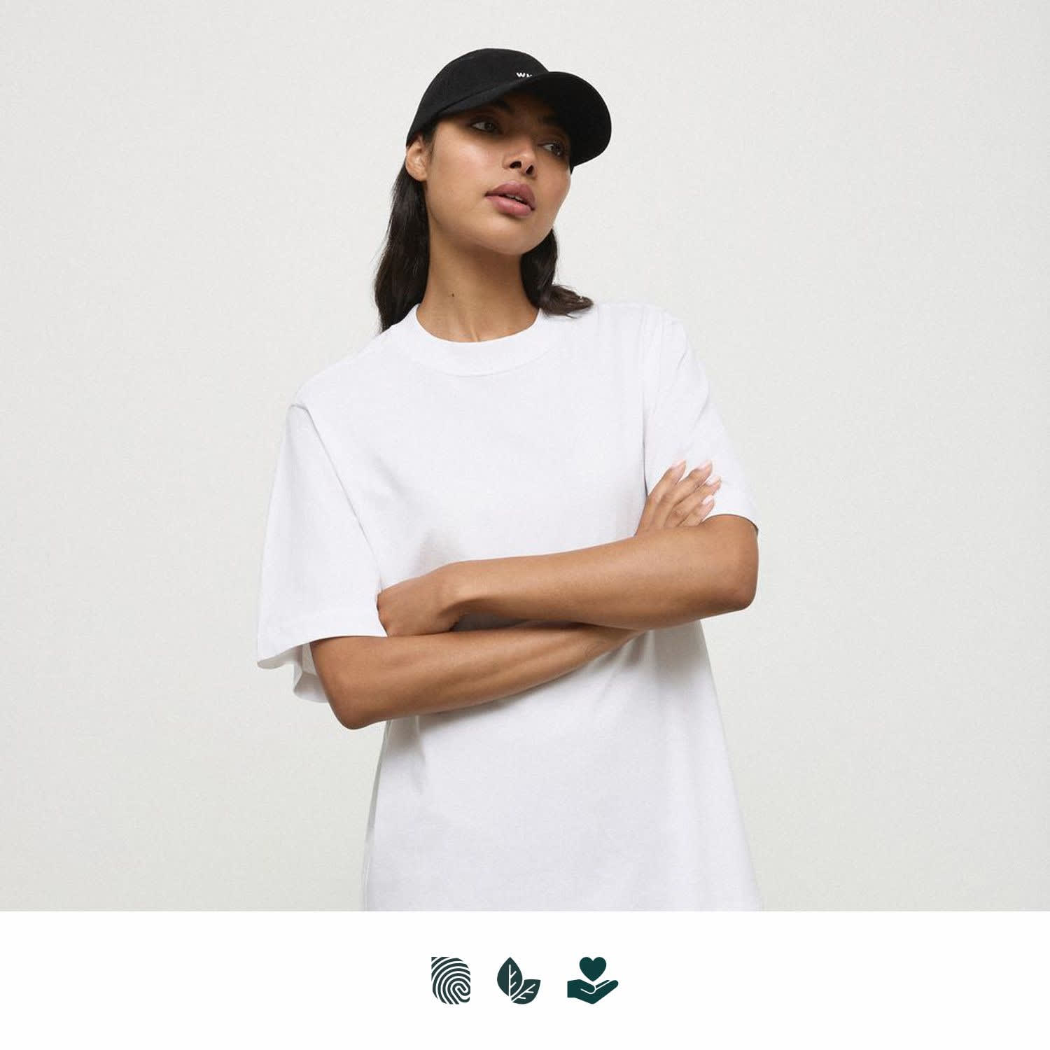 A white t-shirt displayed on a person wearing a black cap. The shirt has a relaxed fit and includes branding. WNSDY Essential Tee - Image 1