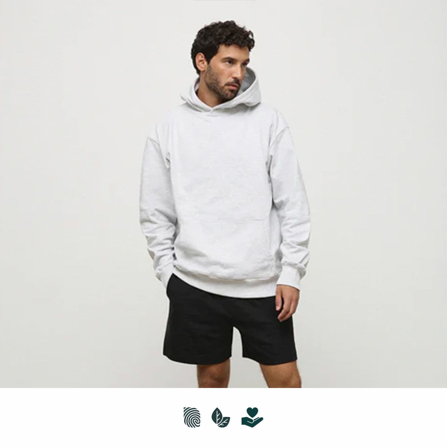 A man wearing a light grey hoodie and black shorts stands against a plain background. The hoodie has a logo. WNSDY Essential Hoodie - Image 1