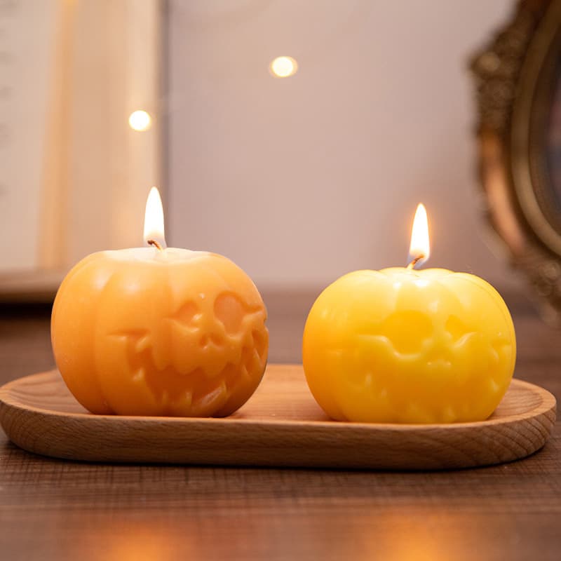 Two pumpkin-shaped candles in orange and yellow, featuring carved faces, displayed on a wooden tray. Pumpkin Shape Candles - Image 1