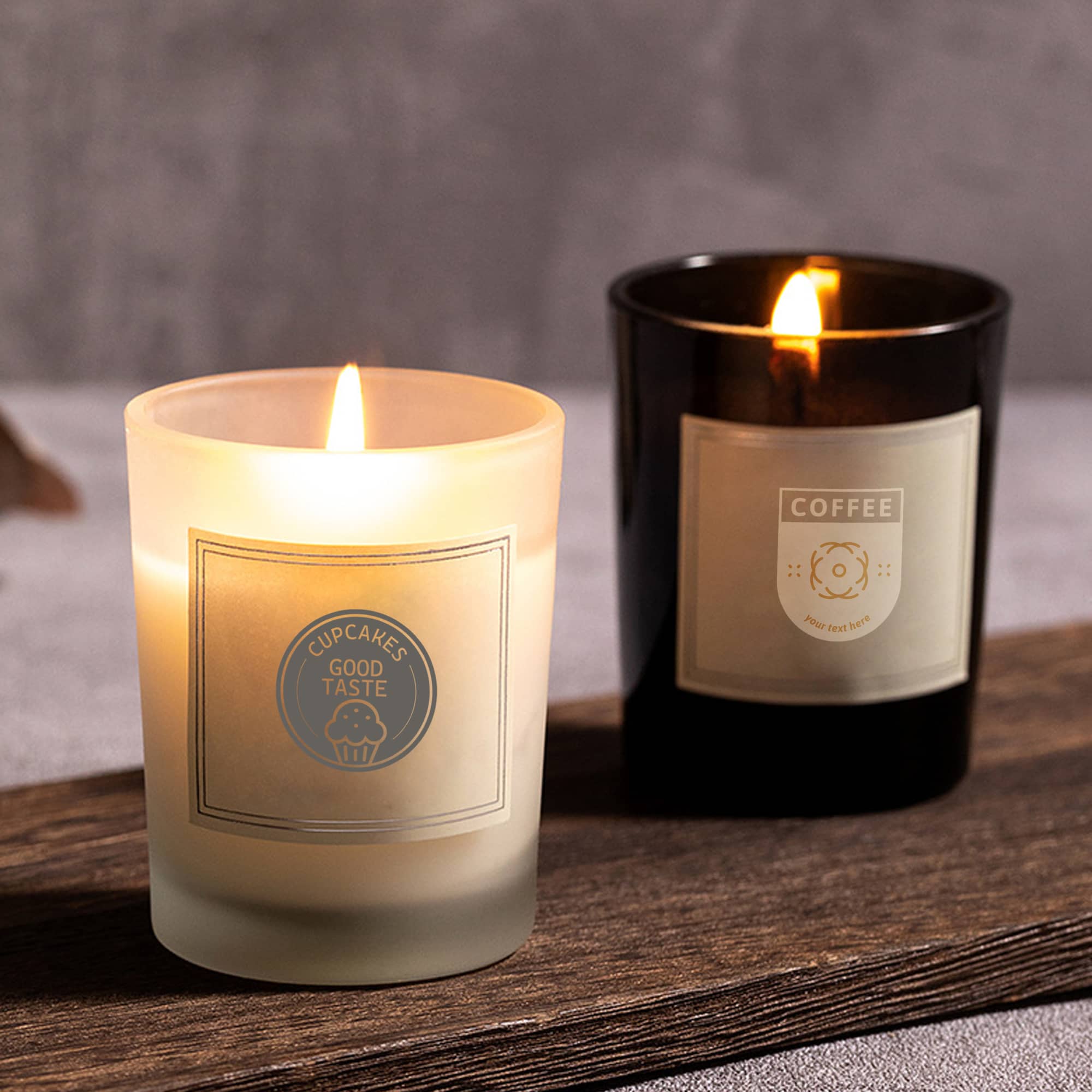 A frosted white candle and a black candle, both lit, sitting on a wooden surface with labels. 2.2oz Glass Candle - Image 1