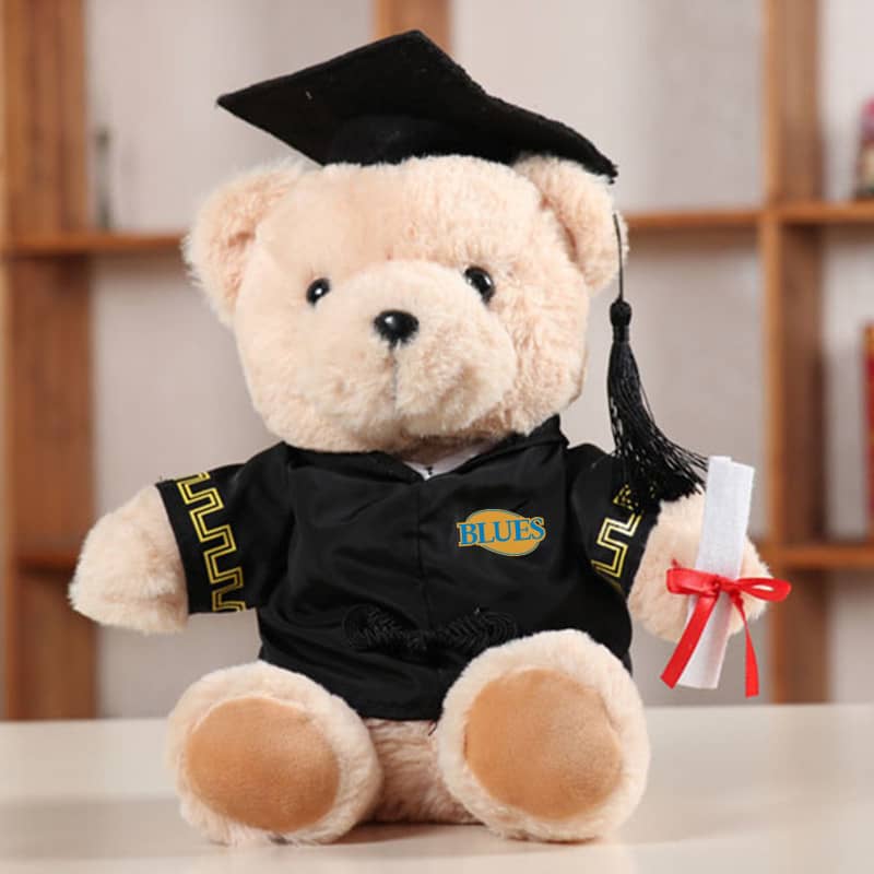 A plush teddy bear dressed in a black graduation gown and cap, holding a rolled diploma with a red ribbon. Graduation Bear Plush Toy - Image 1