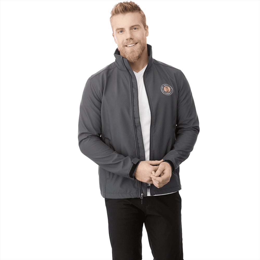 A man wearing a grey softshell jacket with a logo, posing in a casual outfit. Maxson Softshell Jacket - Mens - Image 1