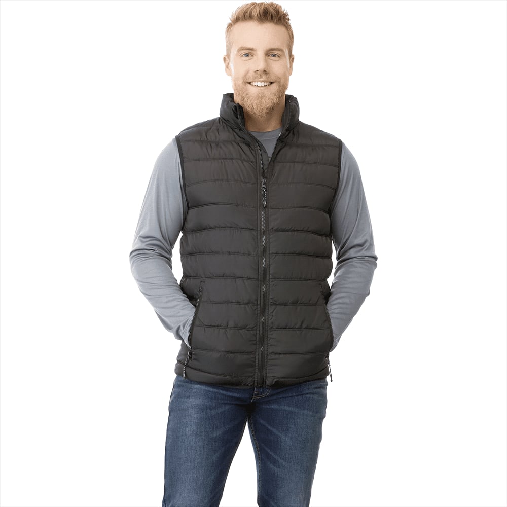 A man wearing a black insulated vest over a grey long-sleeve shirt, smiling and posing. The vest features a logo. Mercer Insulated Vest - Mens - Image 1