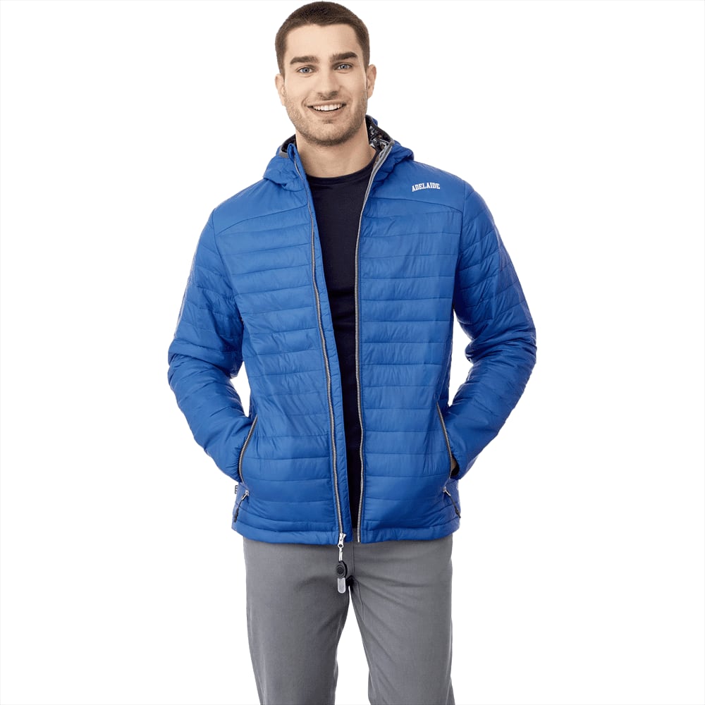 A man wearing a blue packable puffer jacket with a hood, featuring a logo. The jacket is zipped and has side pockets. Silverton Packable Ins Jkt - Mens - Image 1