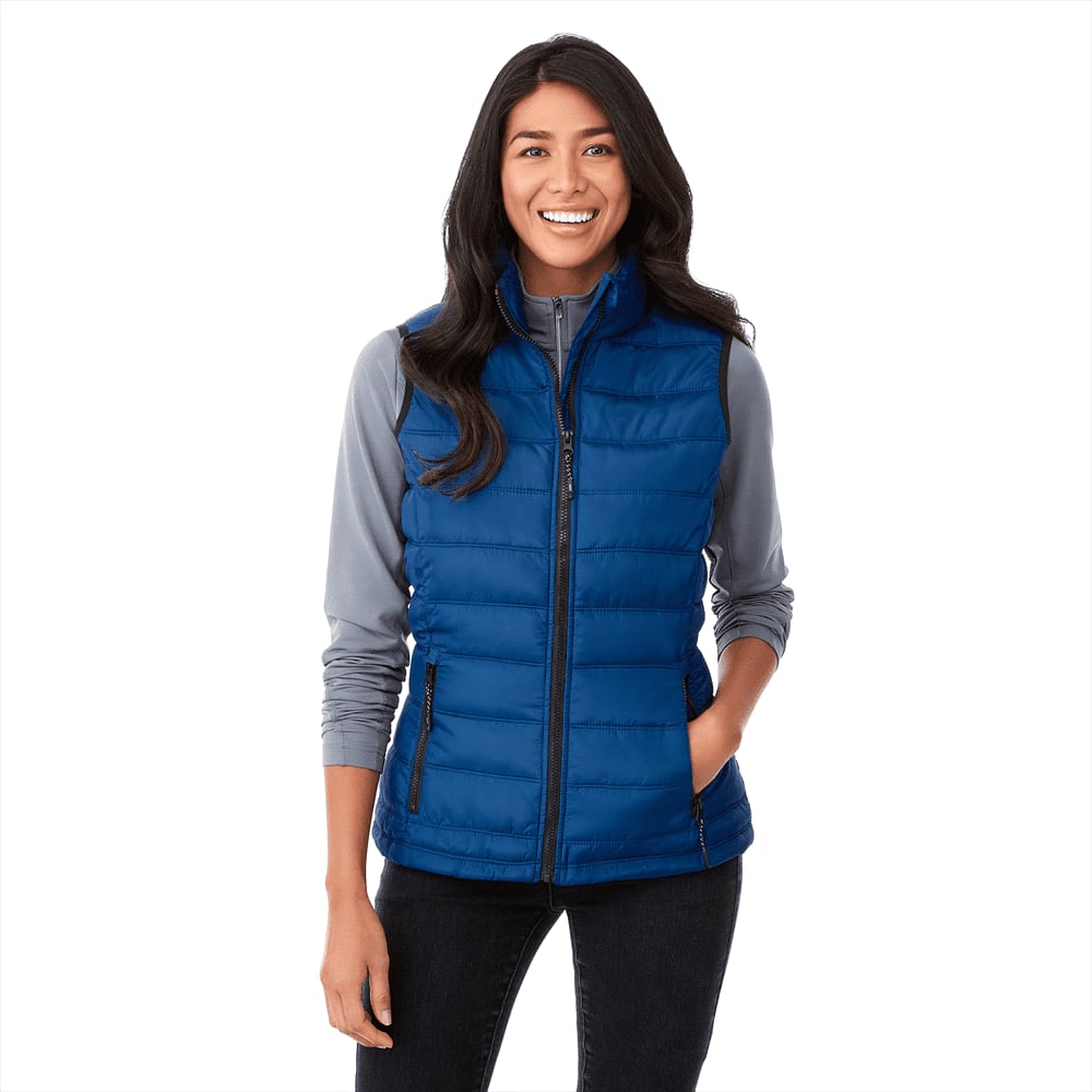 A woman wears a blue insulated vest over a grey long-sleeve top, smiling and posing for the image. Mercer Insulated Vest - Womens - Image 1