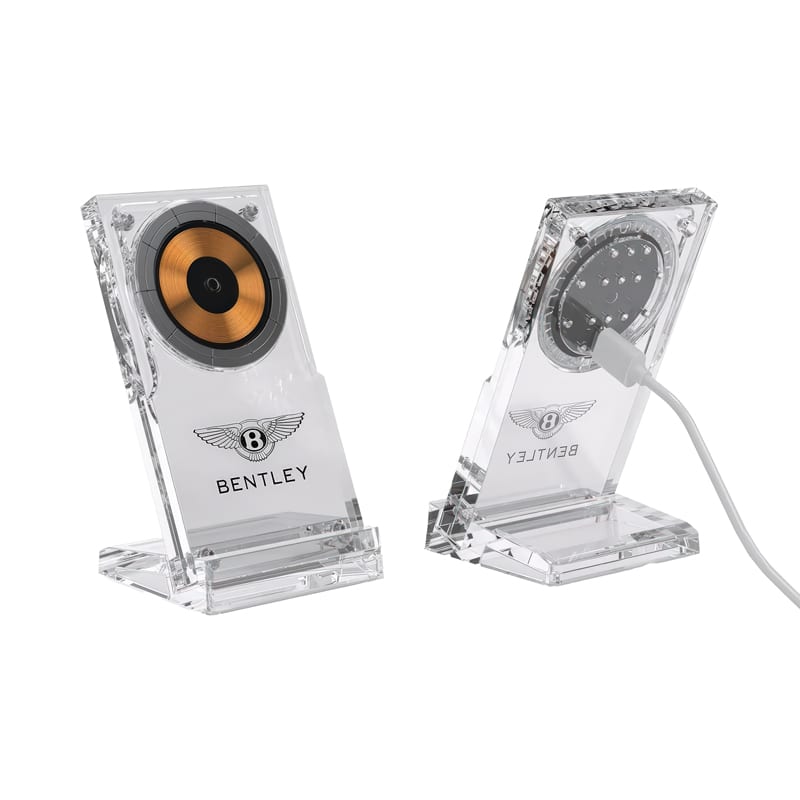 A clear acrylic magnetic wireless charging stand with a gold and black circular charging pad. It features a logo. Norris 15W Acrylic Magnetic Wireless Charging Stand - Image 1