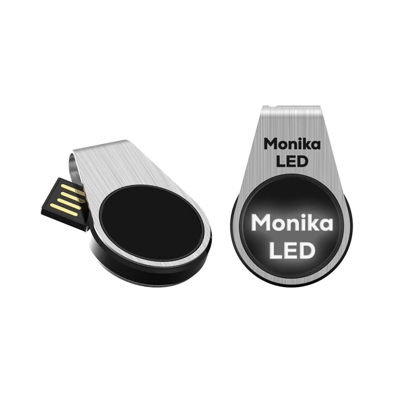 A silver LED flash drive with a black circular section and a branding logo. The drive has a retractable connector. Monika LED Flash Drive - Image 1