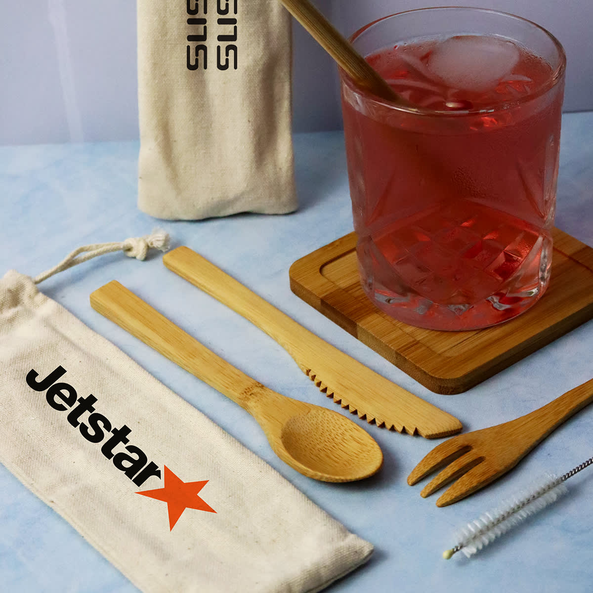 A bamboo cutlery set including a fork, spoon, knife, and cleaning brush, with a drawstring pouch and a drink glass. Adair Bamboo Cutlery Set - Image 1