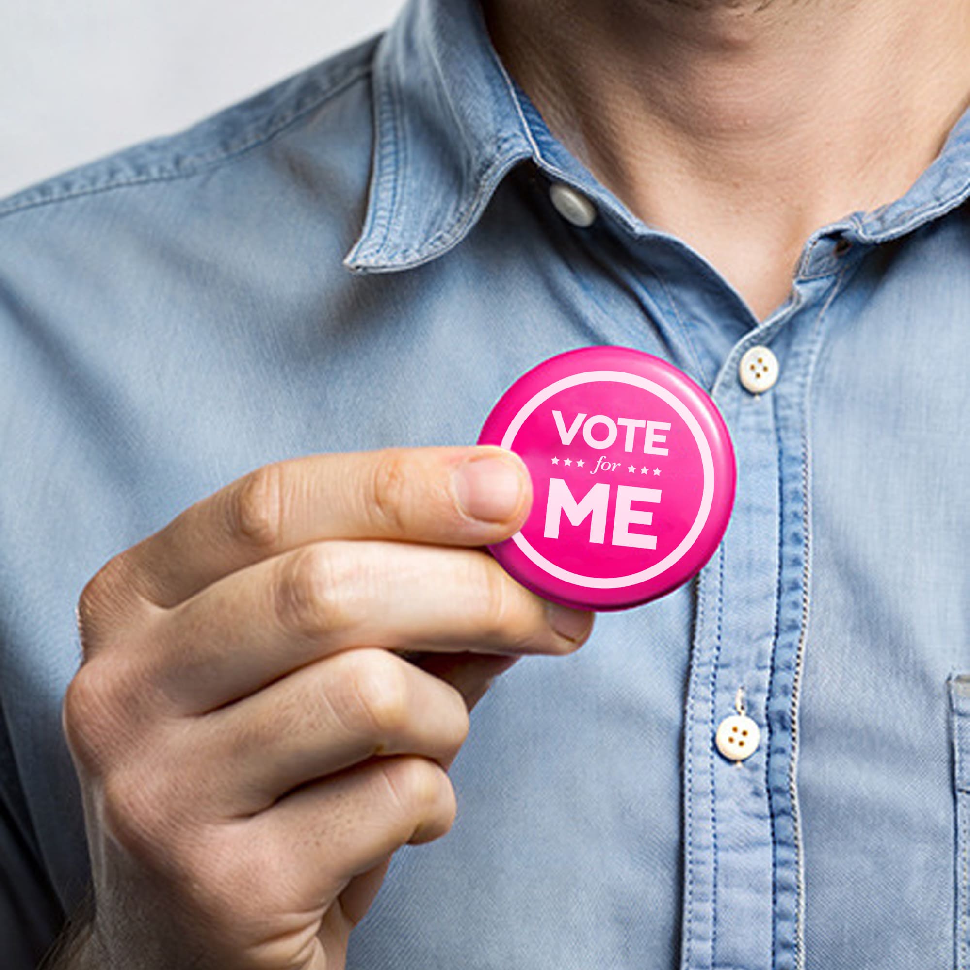 A round pink button badge held by a person wearing a blue collared shirt. The badge features a logo. Button Badge Round 58mm - Image 1