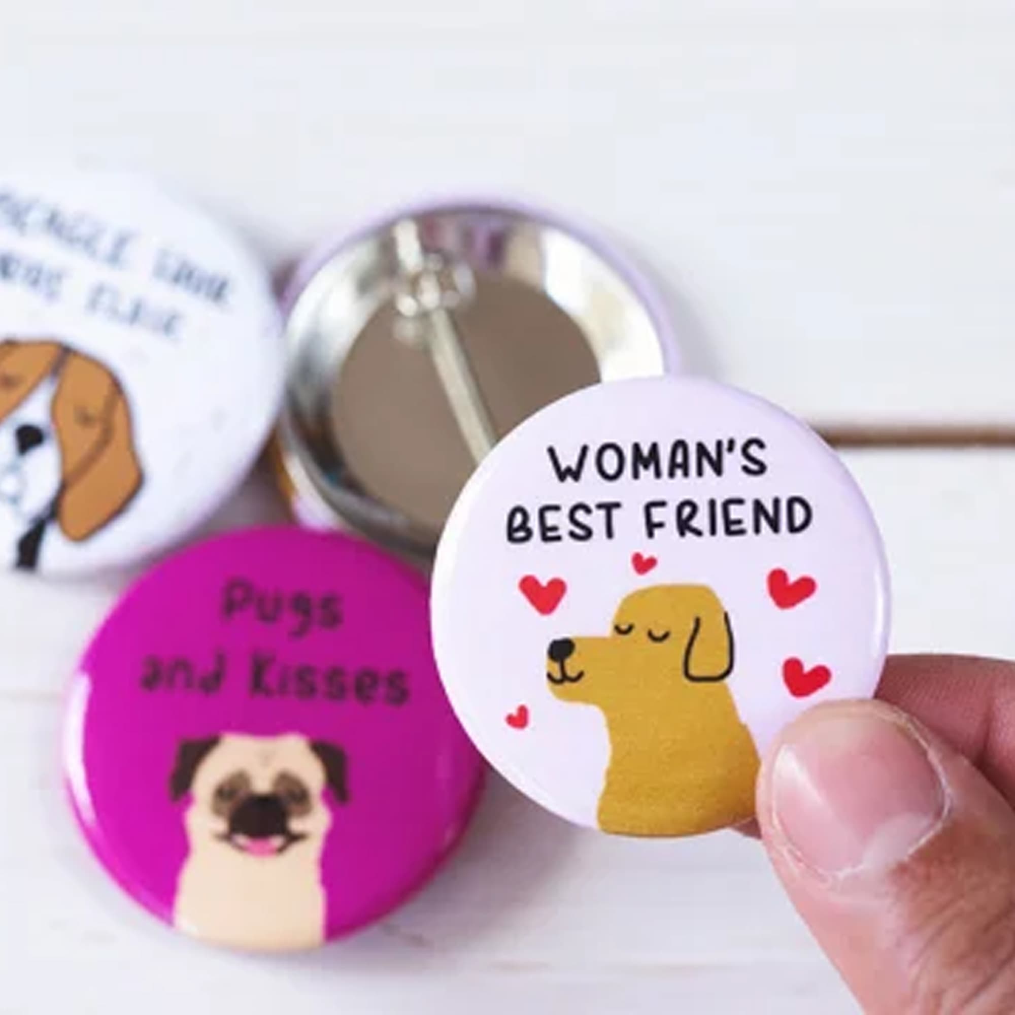 A hand holds a round, 25mm button badge featuring a dog illustration on a pink background, among other badges. Button Badge Round 25mm - Image 1