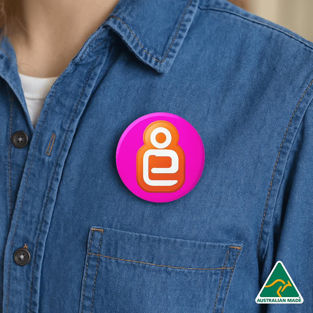 A 32mm button badge featuring vibrant pink and orange colours, worn on a denim shirt with a logo in the corner. Button Badge 32mm - Image 1