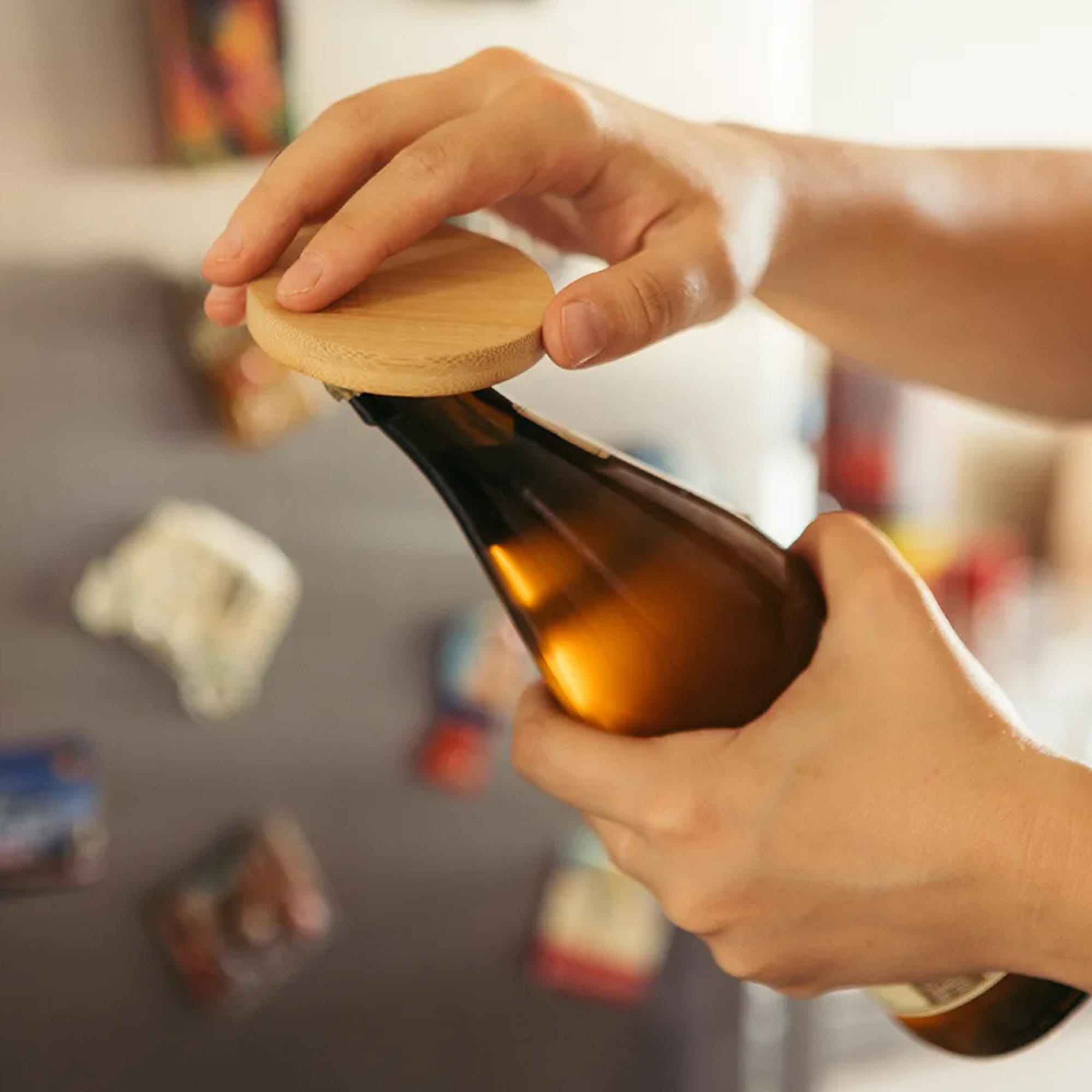 A drink bottle opener made of bamboo, featuring a circular design and held by a hand, with a dark bottle in view. Bamboo Bottle Opener - Image 1