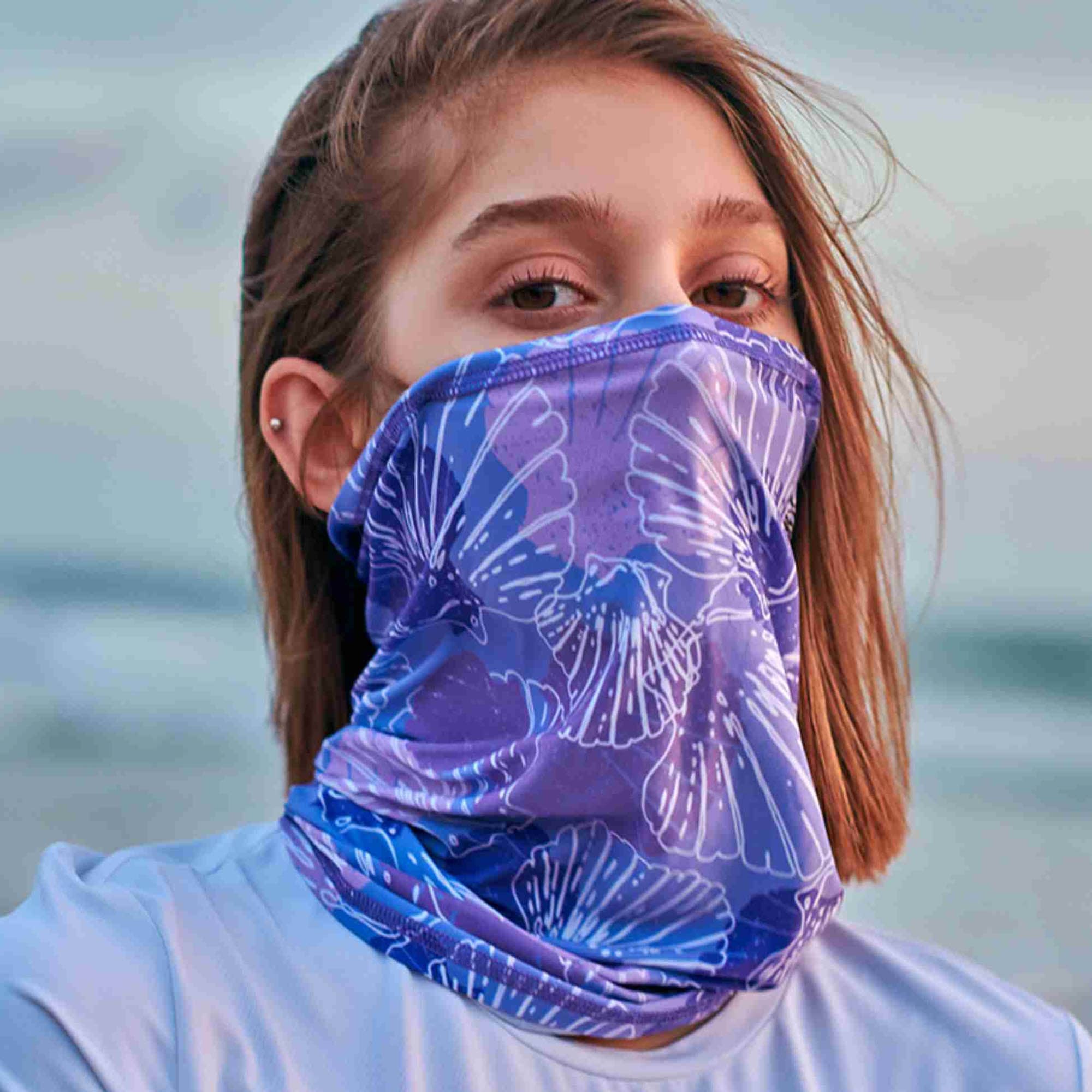 A purple bandana with a floral pattern, worn as a face covering by a person. It features a branding logo. Coolmax Bandana – Adult Large - Image 1