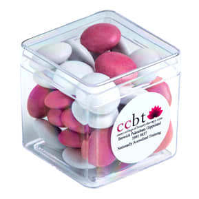 A clear cube container filled with pink and white chocolate-coated beans. The container has a label and branding. Hard Cube with Choc Beans 40g - Image 1