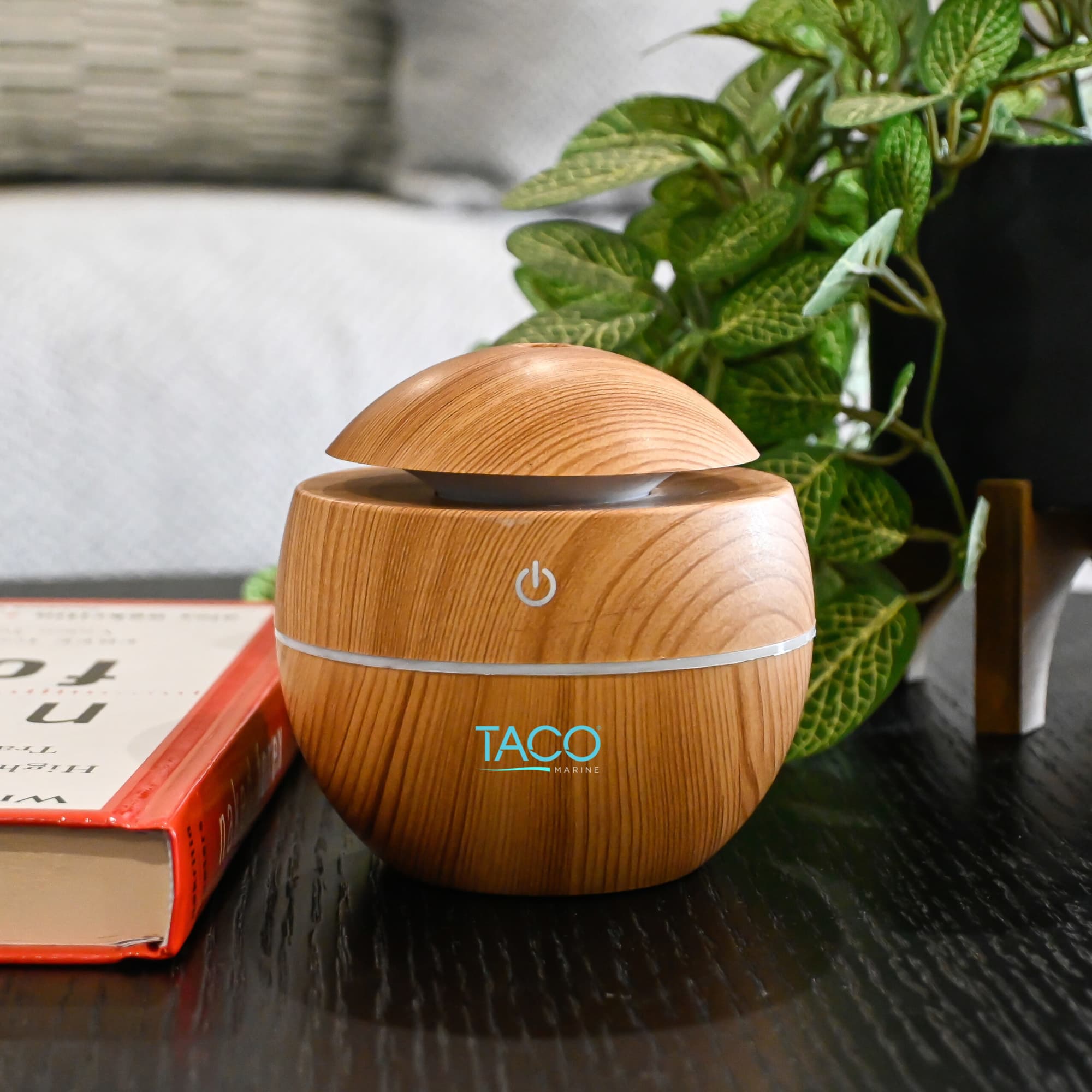A wooden-patterned diffuser with a rounded design on a dark table, surrounded by greenery and a book. Breathable Bliss Diffuser - Image 1