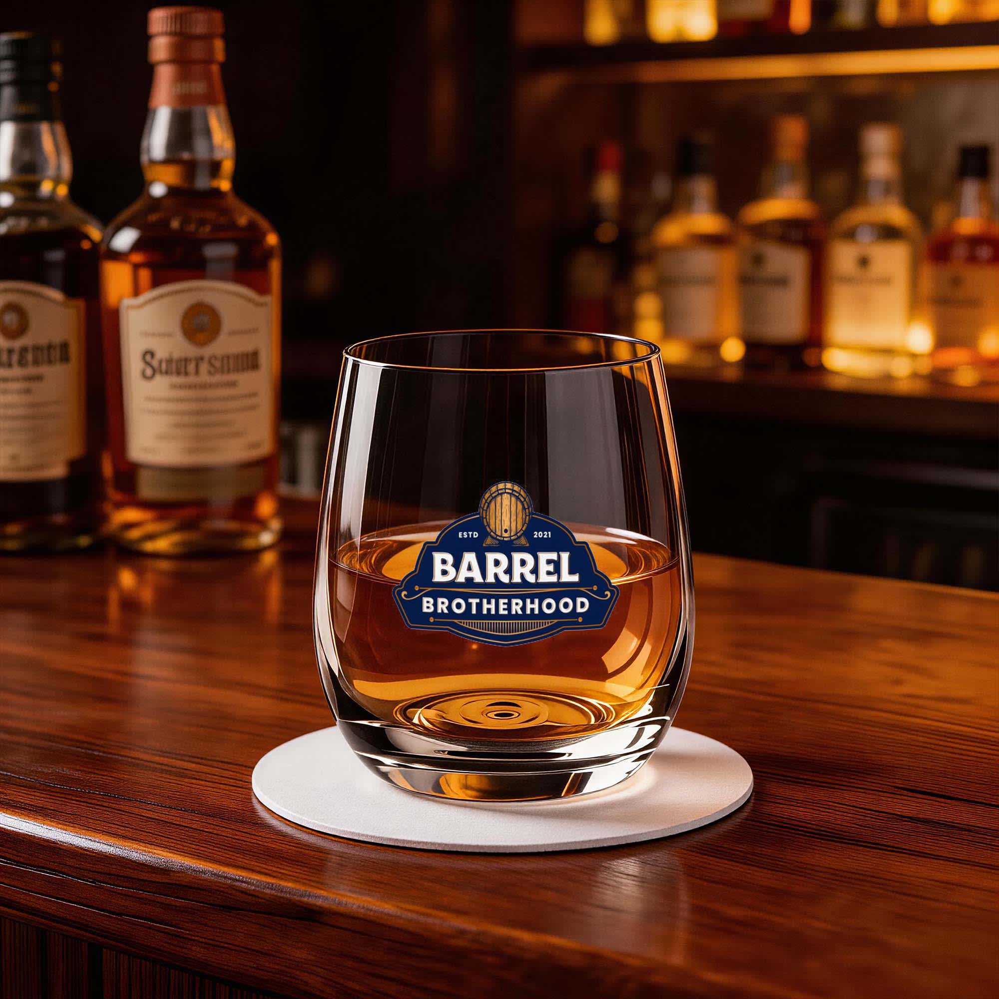 A stemless glass cup filled with amber liquid, featuring a logo, sitting on a bar counter. Bomia Stemless Glass Cup 345ml - Image 1