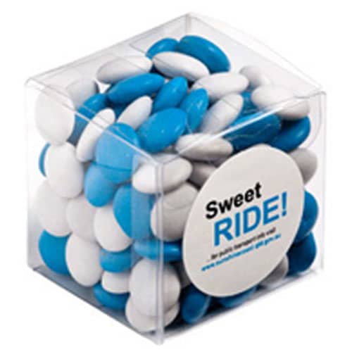 A clear cube filled with blue and white chocolate beans, with a circular branding logo on the front. Cube with Choc Beans 110g - Image 1