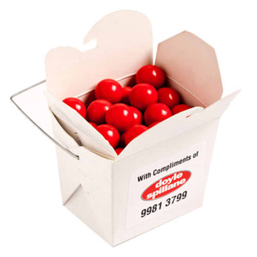 A white cardboard noodle box filled with bright orange chocolate drops. The box has a handle and a branding logo. White Cardboard Noodle Box with Orange Choc Drops 100g - Image 1