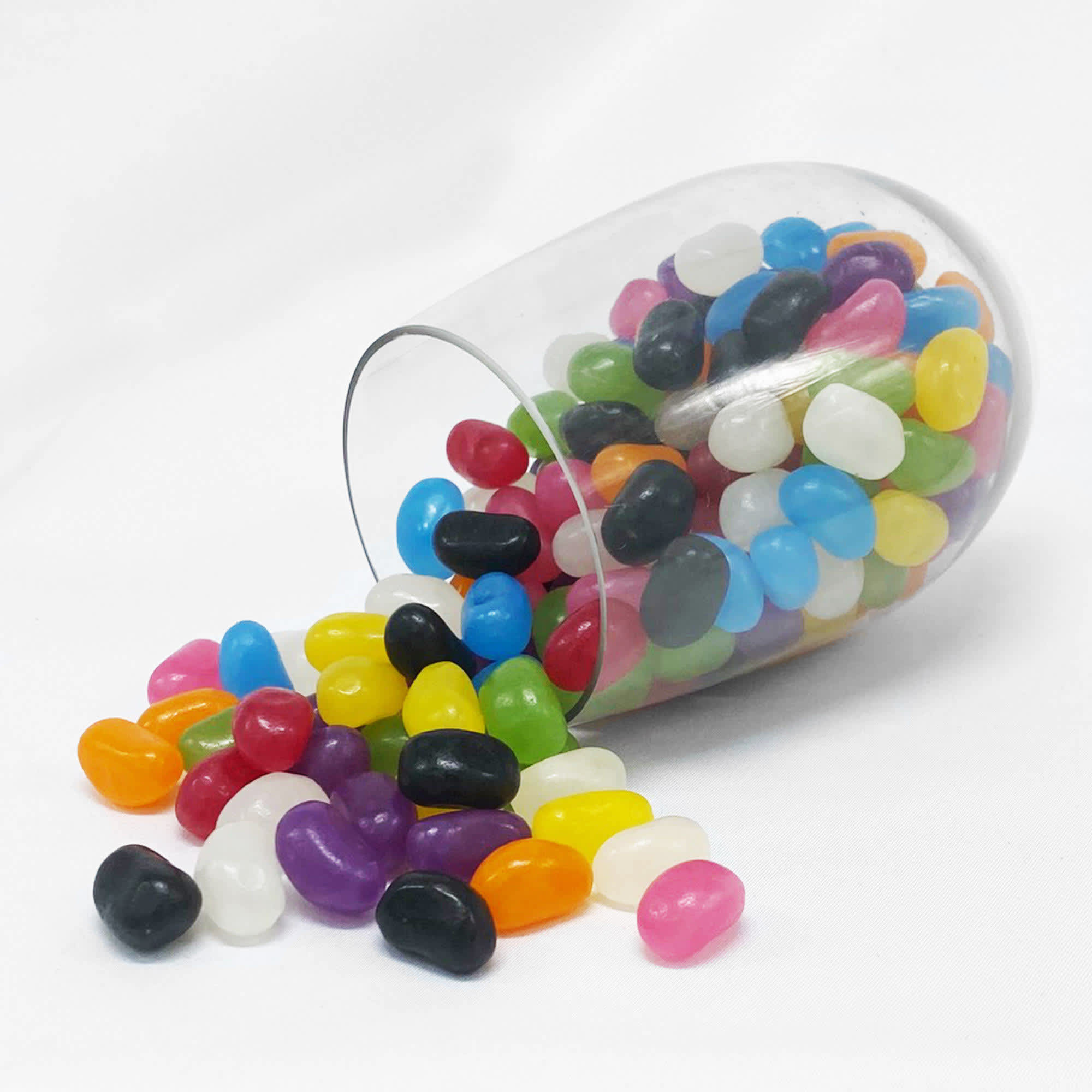 A clear crystal PET cup with an assortment of vibrant jelly beans in various colours, some spilling out. Jelly Bean In Crystal PET Cup - Image 1