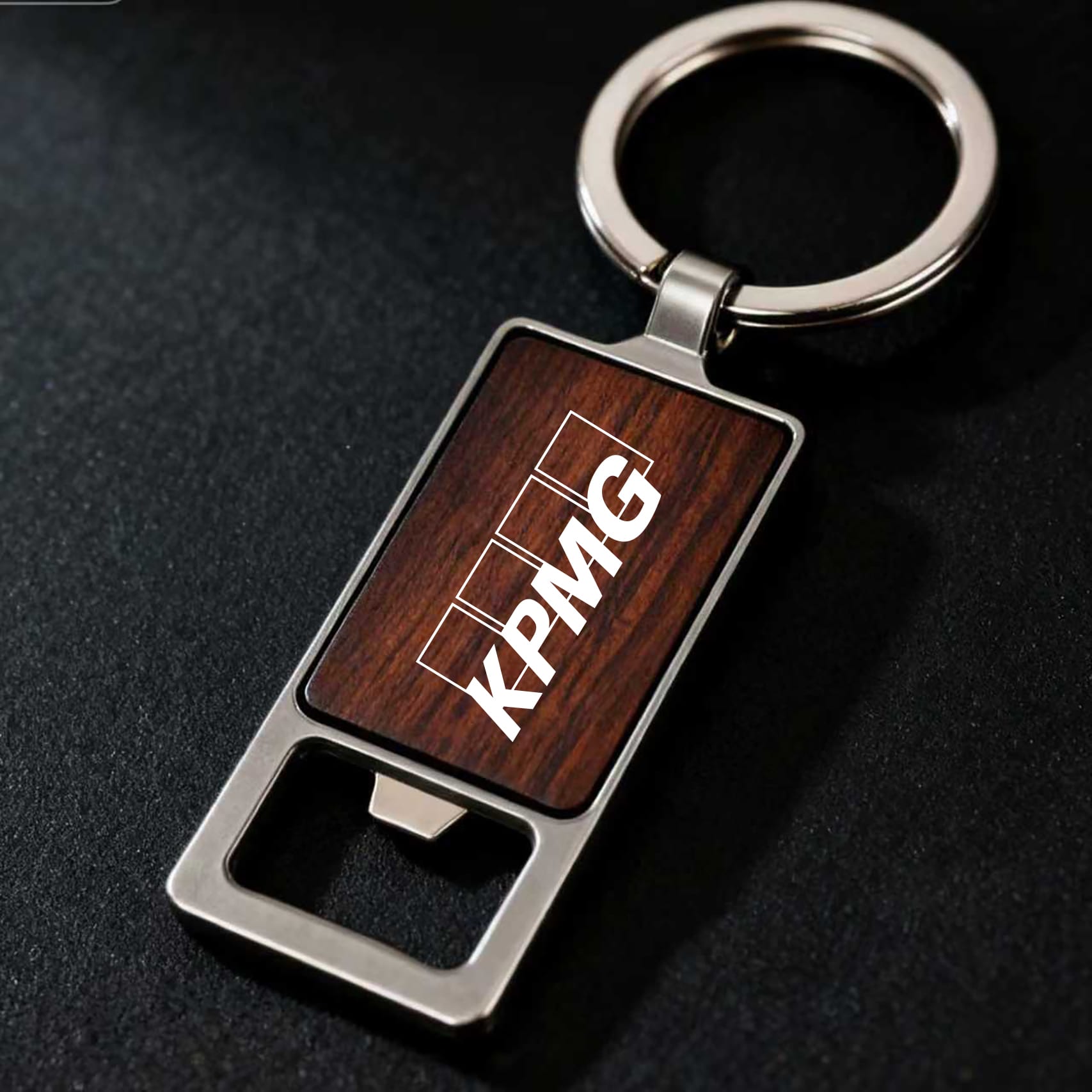 A drink bottle opener keyring featuring a square wooden design and a silver metal keyring, with a logo. Autumn Wood Bottle Opener – Square - Image 1