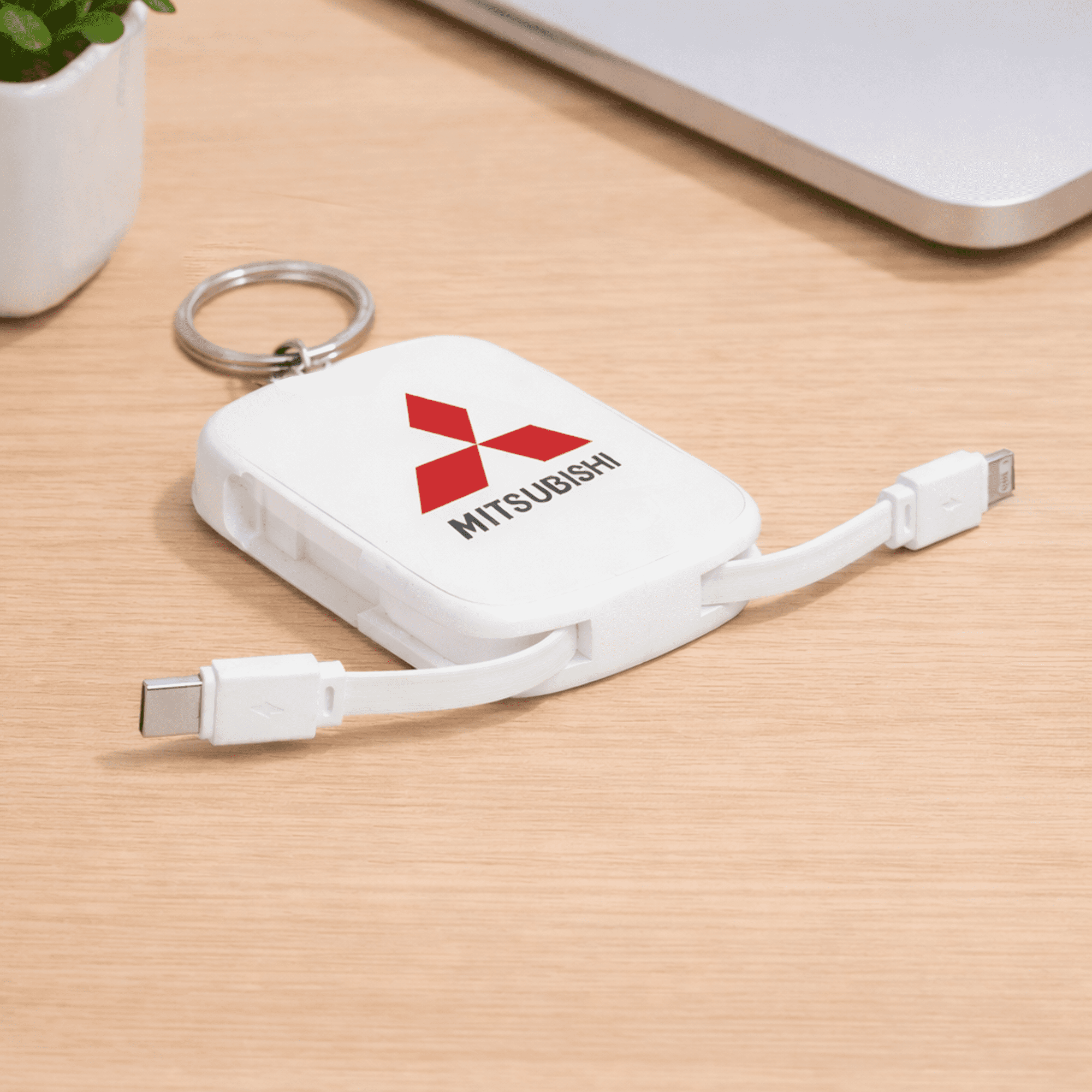 A white power bank keychain with dual charging cables and a logo, resting on a wooden surface next to a laptop. Neo Keychain Powerbank 2000mAh - Image 1