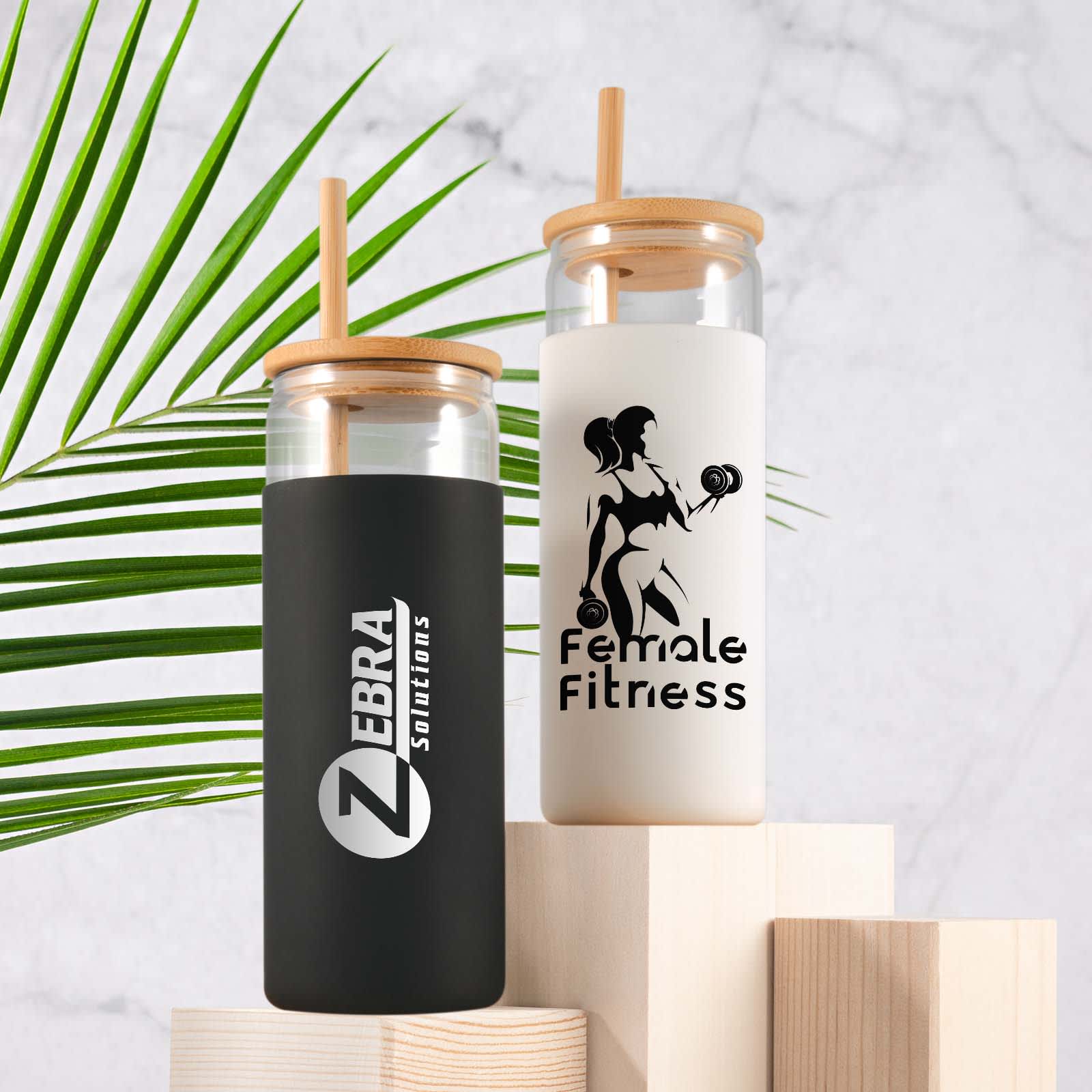 A set of two glass tumblers with bamboo lids, one black and one white, featuring logos and designs. Pisa Glass Tumbler - Image 1