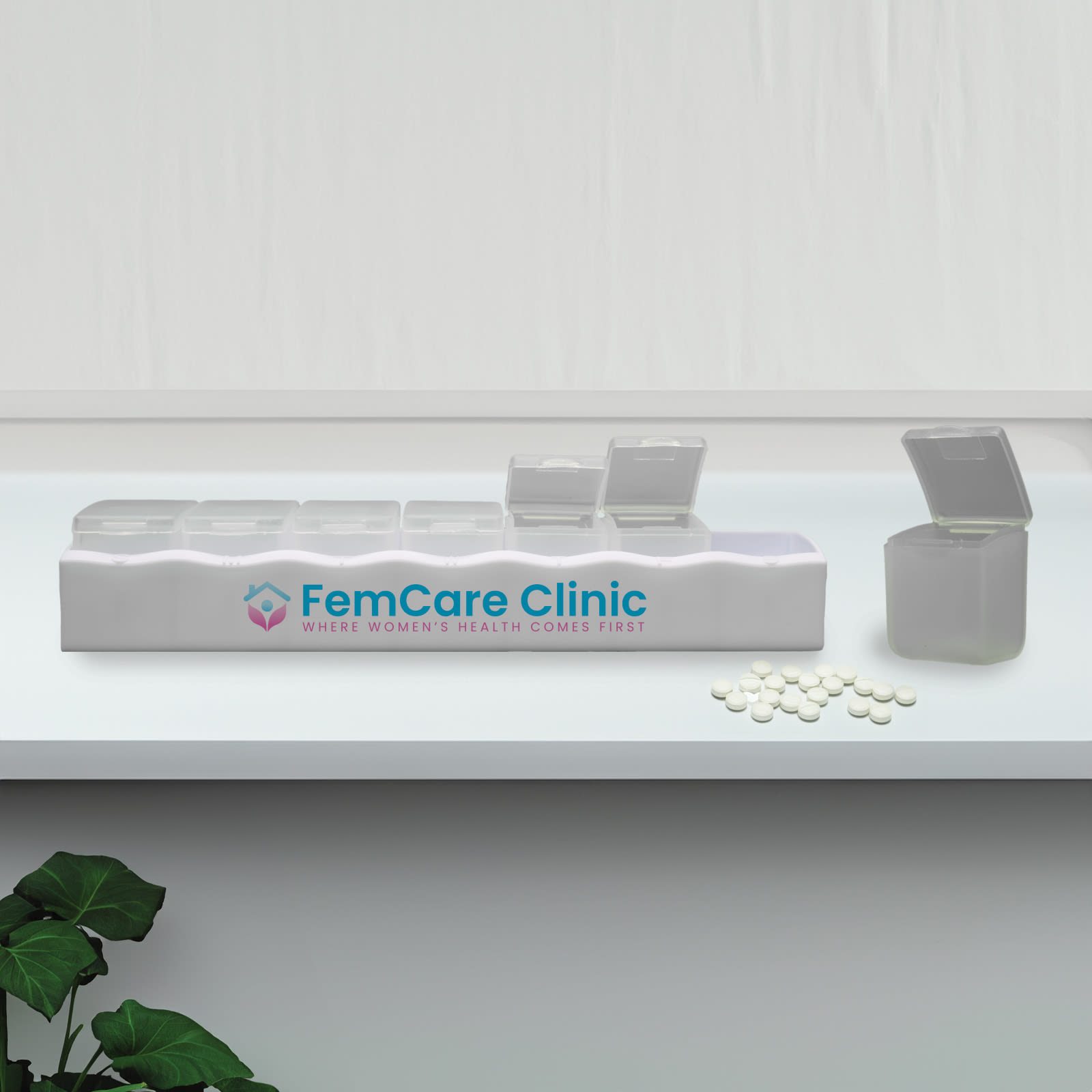 A white weekly pill box with multiple compartments, some open, alongside white pills and a plant. It has a logo. Weekly Pill Box - Image 1