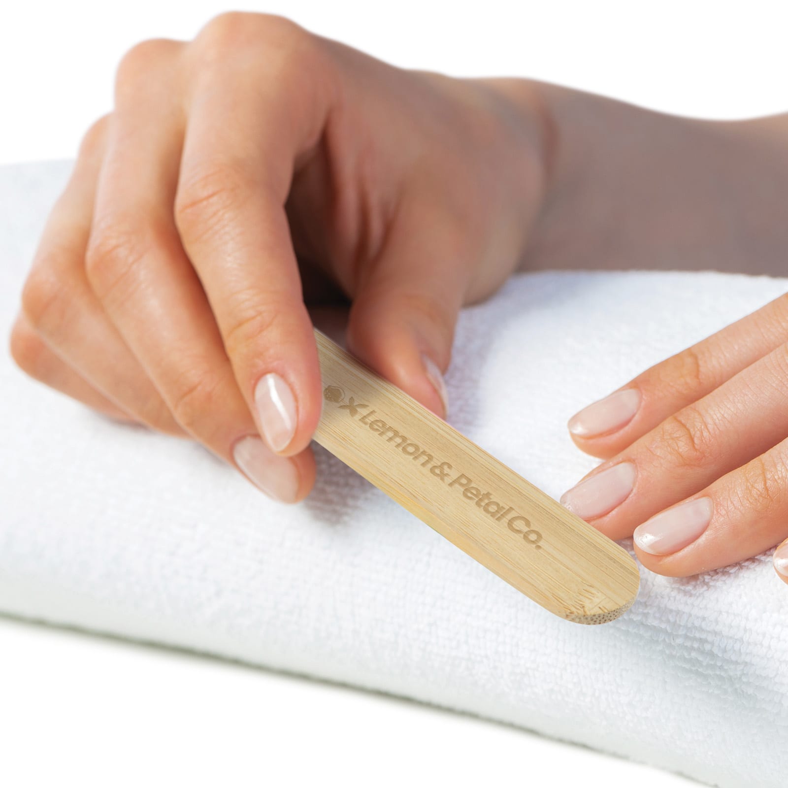 A bamboo nail file held in a hand, resting on a white towel, with natural-looking nails. It features branding. Pamper Bamboo Nail File - Image 1