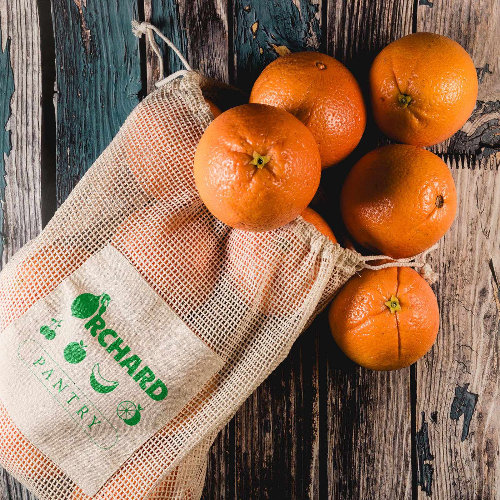 A mesh produce bag containing multiple oranges, with the words "Orchard Pantry" printed on the side. Byron Mesh Produce Bag - Image 1