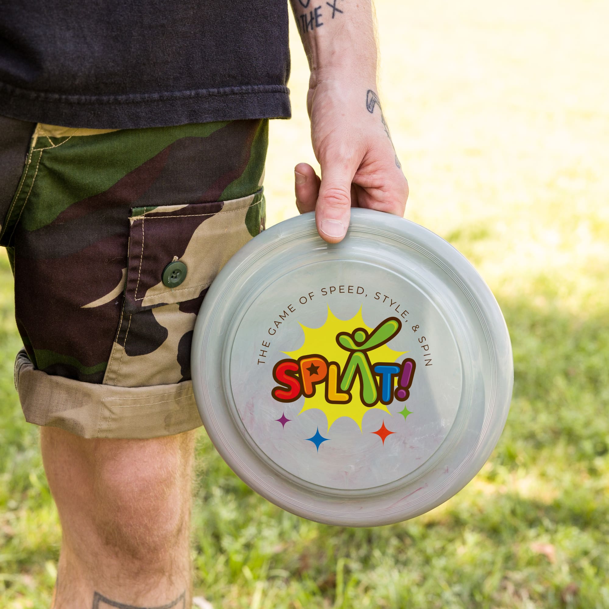 A person holds a translucent gray frisbee featuring colorful text and a logo. The background shows green grass. Aussie Recycled Flyer - Image 1