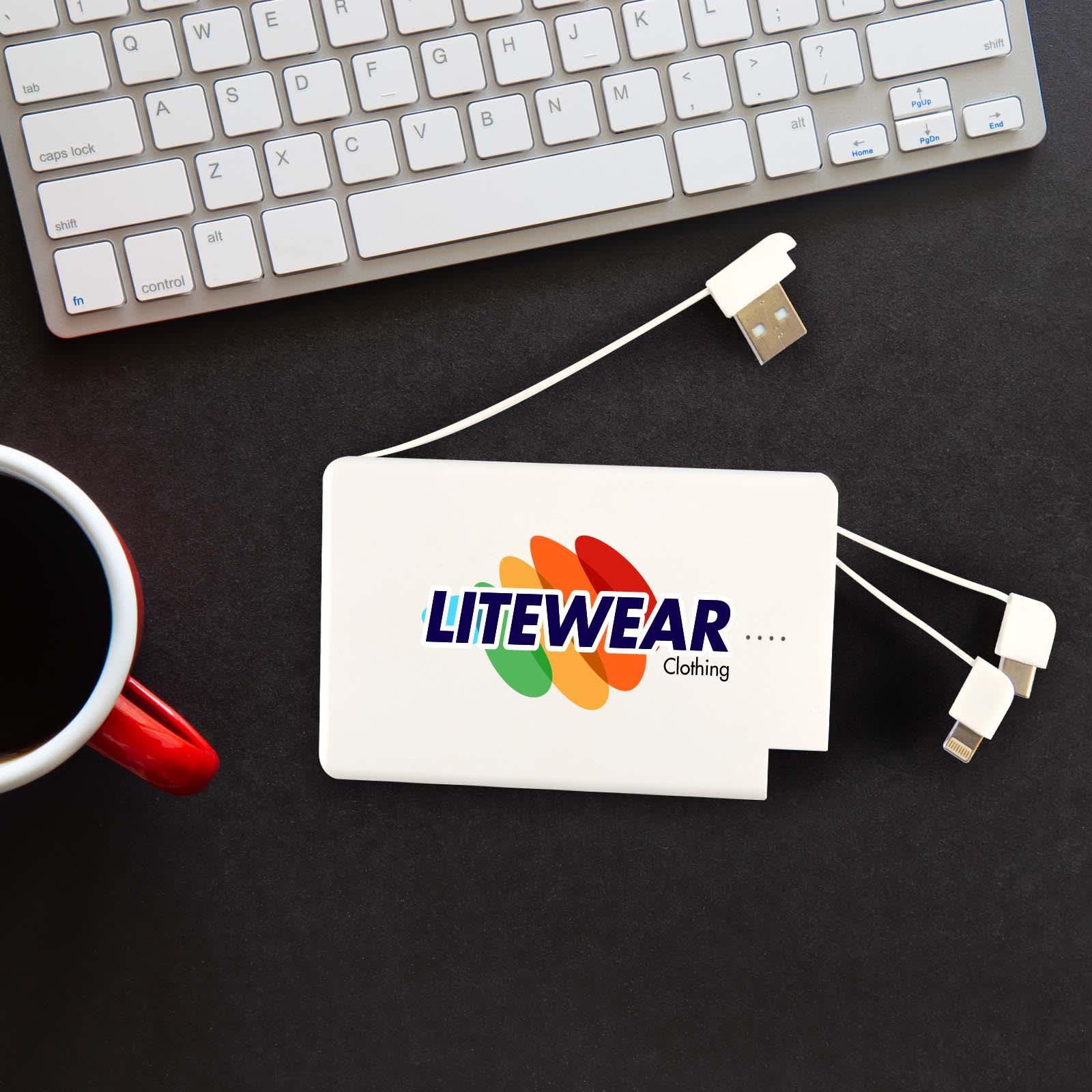 A white power bank with multiple charging cables next to a computer keyboard and a red mug. It has a logo. Arya 5,000mAh Power Bank - Image 1