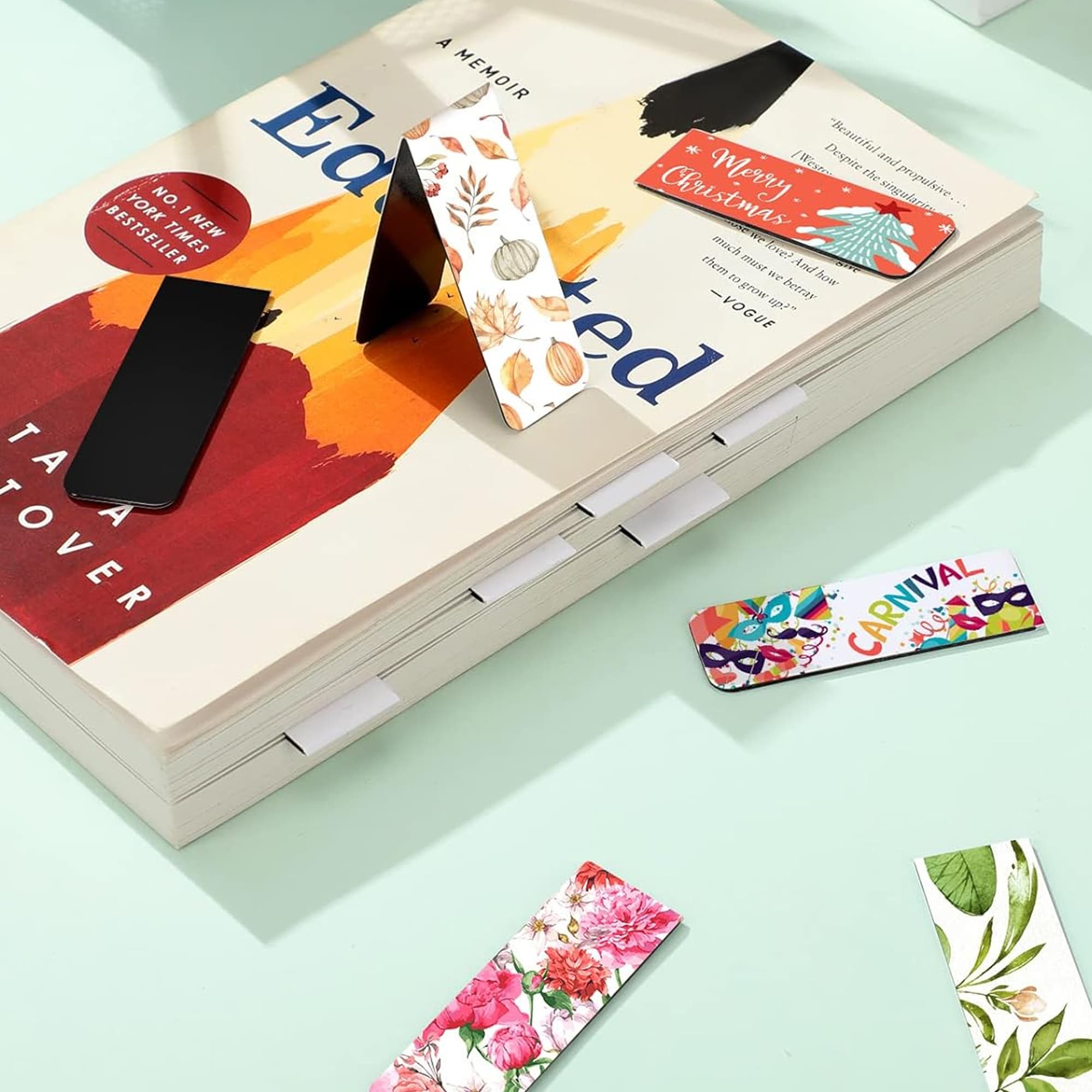 A collection of large bookmarks featuring various vibrant floral and festive designs, placed on a book. Fridge Magnet and Book Mark – Large - Image 1