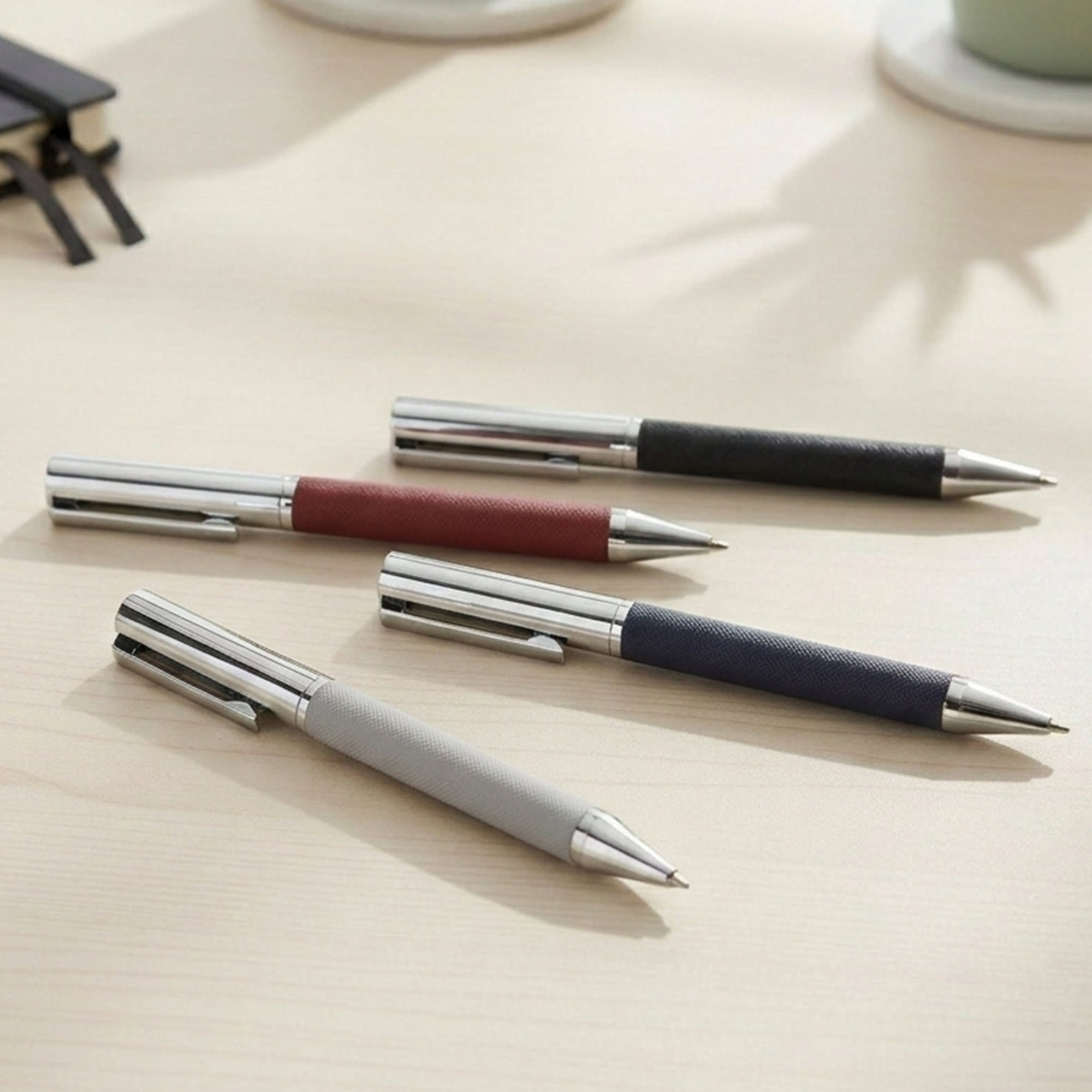 A collection of Geneva Metal Pens in grey, maroon, navy, and black with stainless steel accents, arranged on a desk. Geneva Metal Pen - Image 1