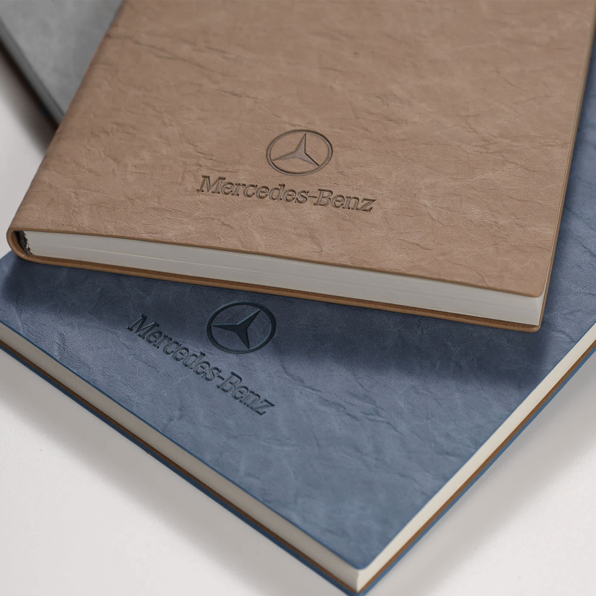 A brown and a blue notebook stacked, featuring a logo. Both have a textured cover and a simple design. Falby Notebook - Image 1