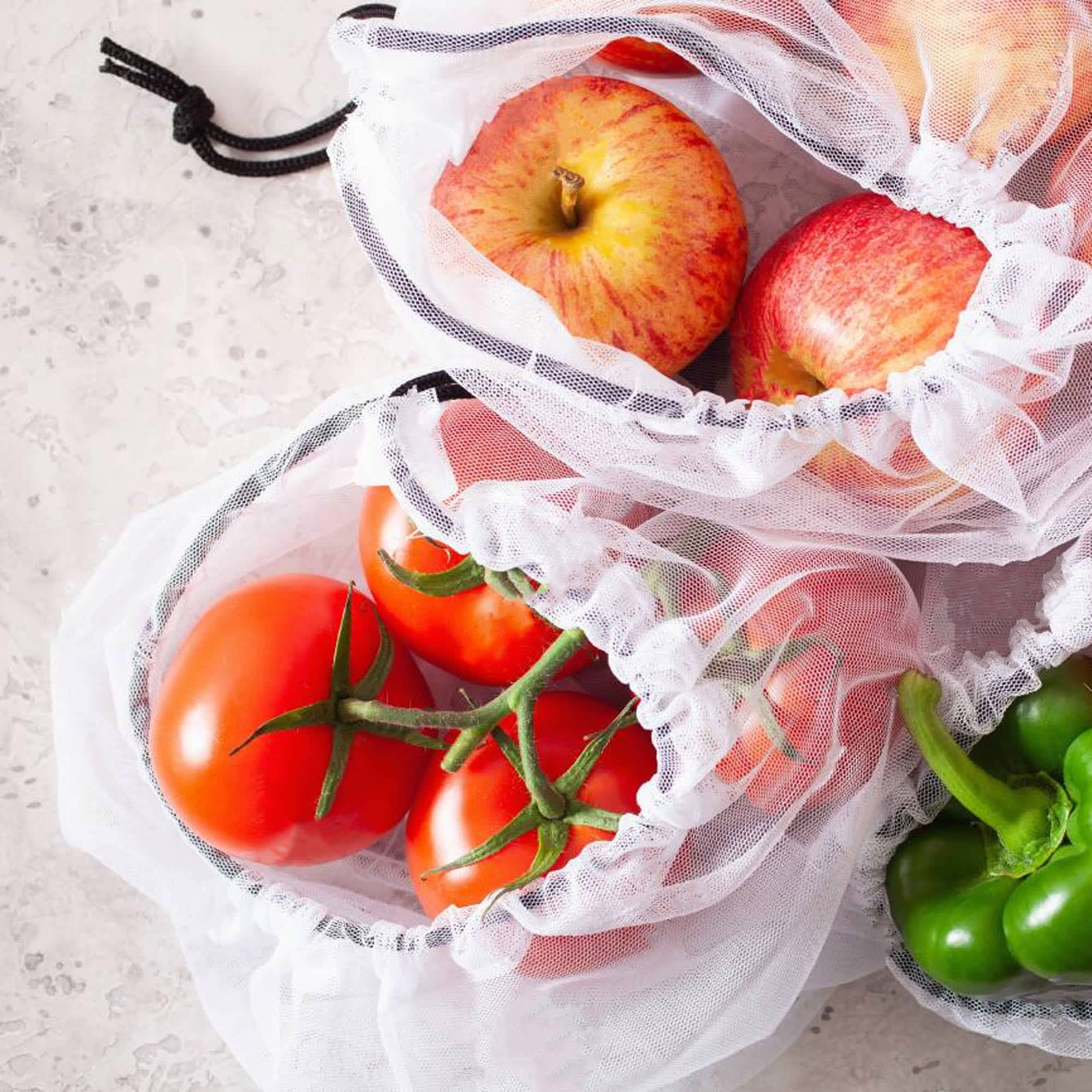 Nylon mesh produce bags containing red apples, ripe tomatoes, and green bell peppers on a textured surface. Nylon Mesh Produce Bag - Image 1