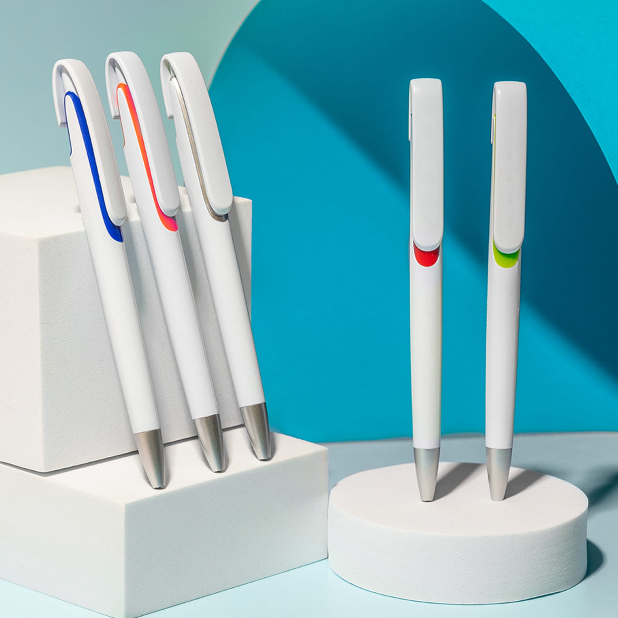A set of five plastic pens in white with coloured accents in blue, orange, green, and red, displayed on white pedestals. Tahlia White - Image 1