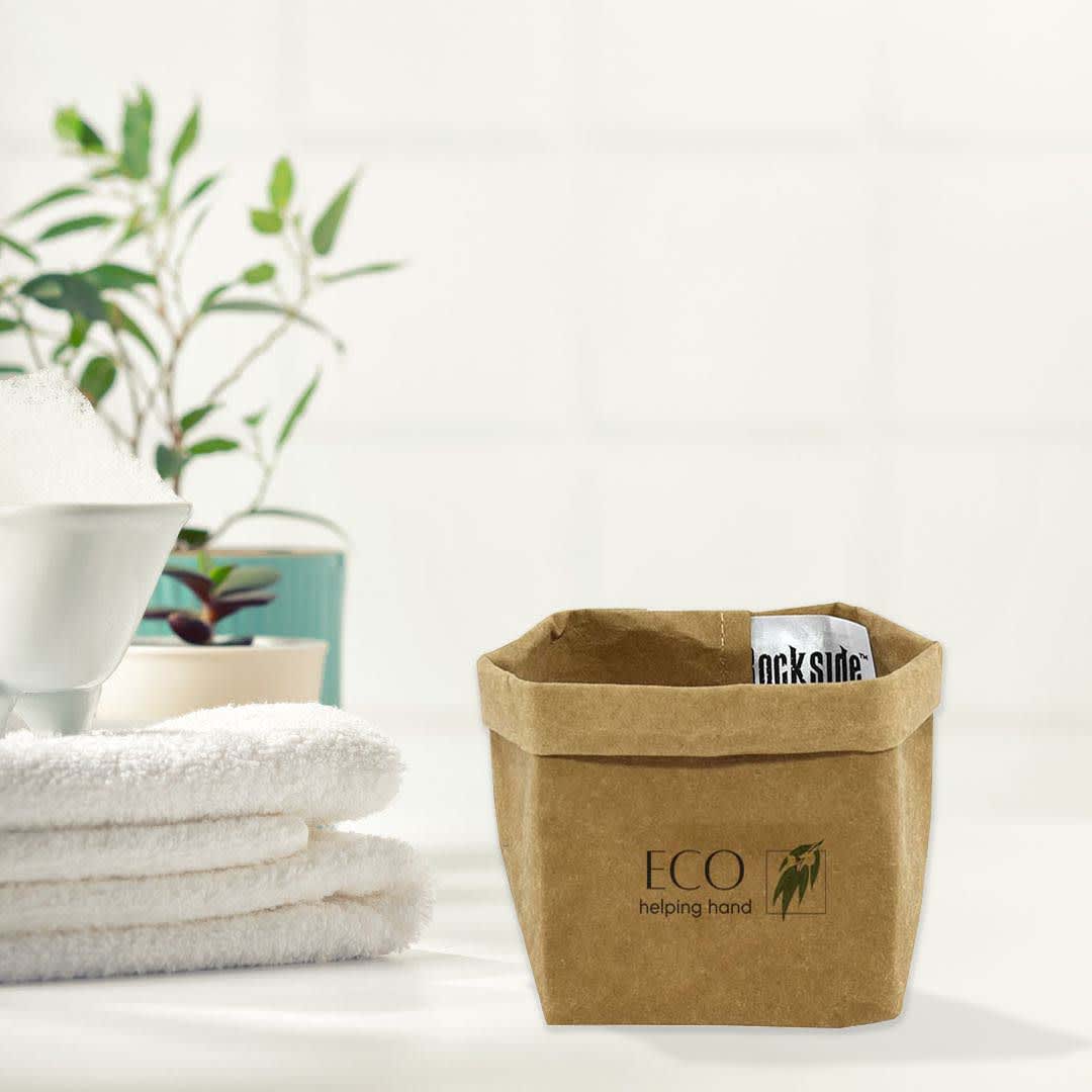 A small brown kraft paper storage bag with a logo, placed beside neatly folded white towels and a green plant. Sewo Kraft Paper Storage Bag – Small - Image 1