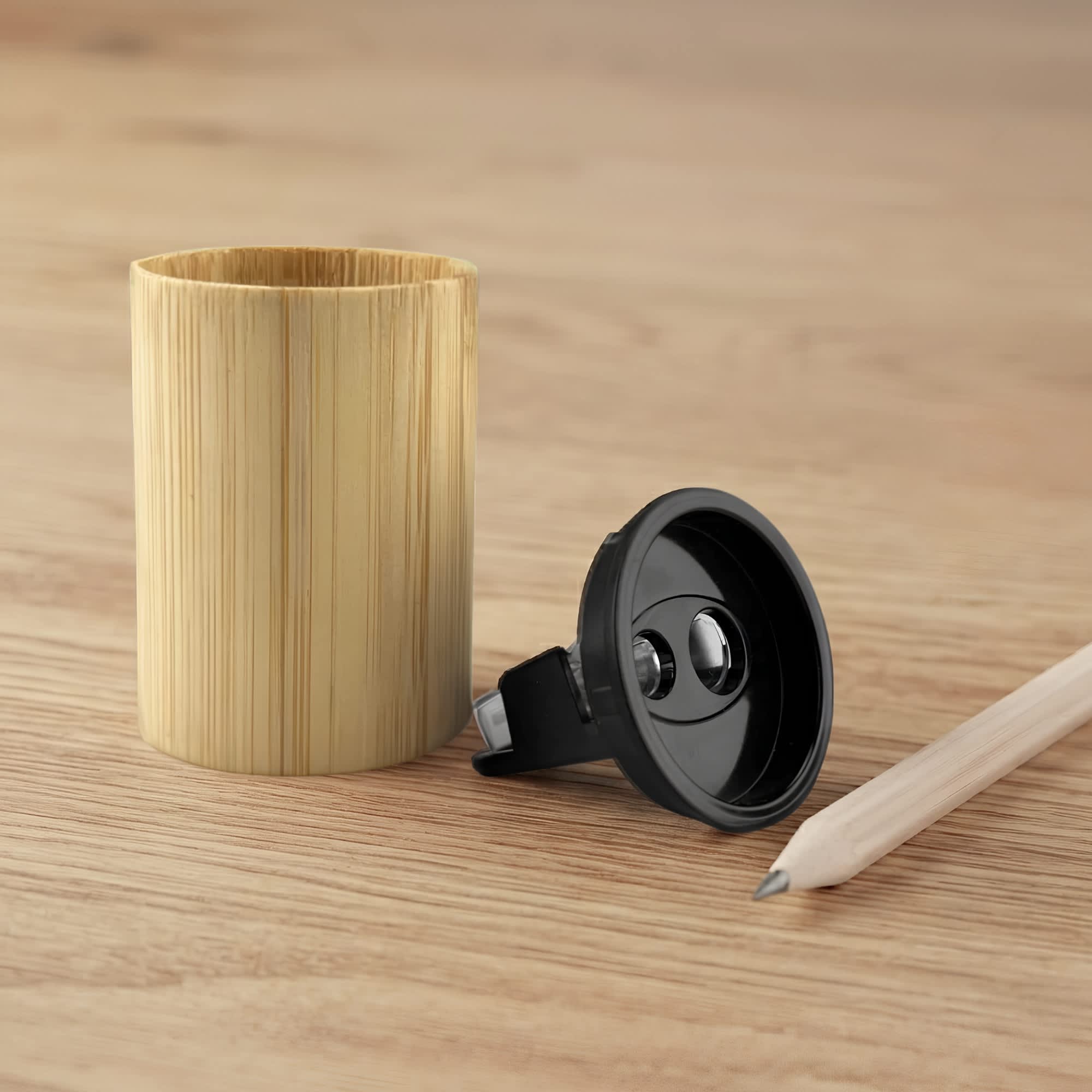 A bamboo pencil sharpener in a cylindrical shape, with a black sharpening mechanism and a light-coloured wooden pencil beside it. Bamboo Pencil Sharpener - Image 1