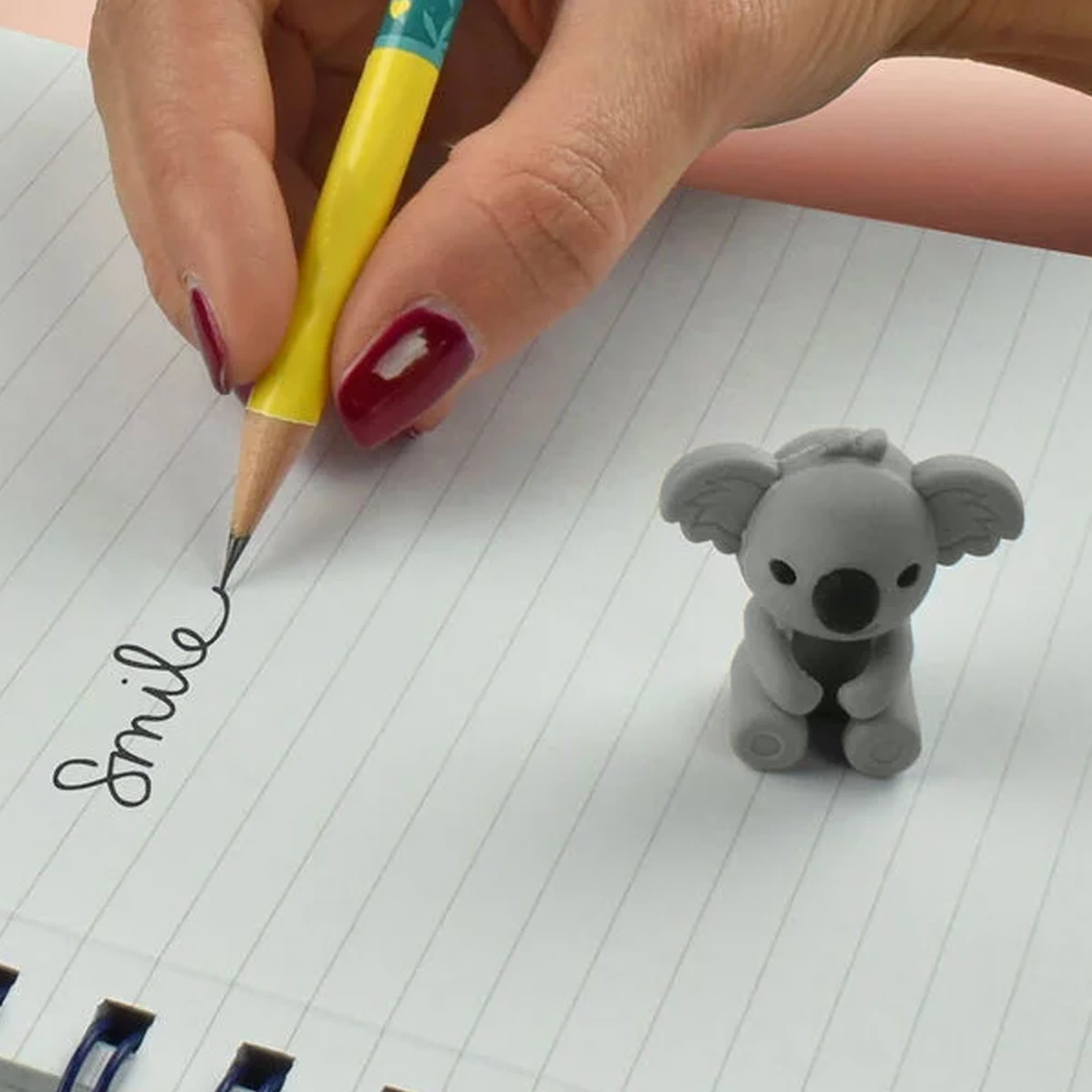 A grey koala-shaped pencil-top eraser next to a yellow pencil, with the word "Smile" written on lined paper. Koala Pencil-Top Rubber Eraser - Image 1