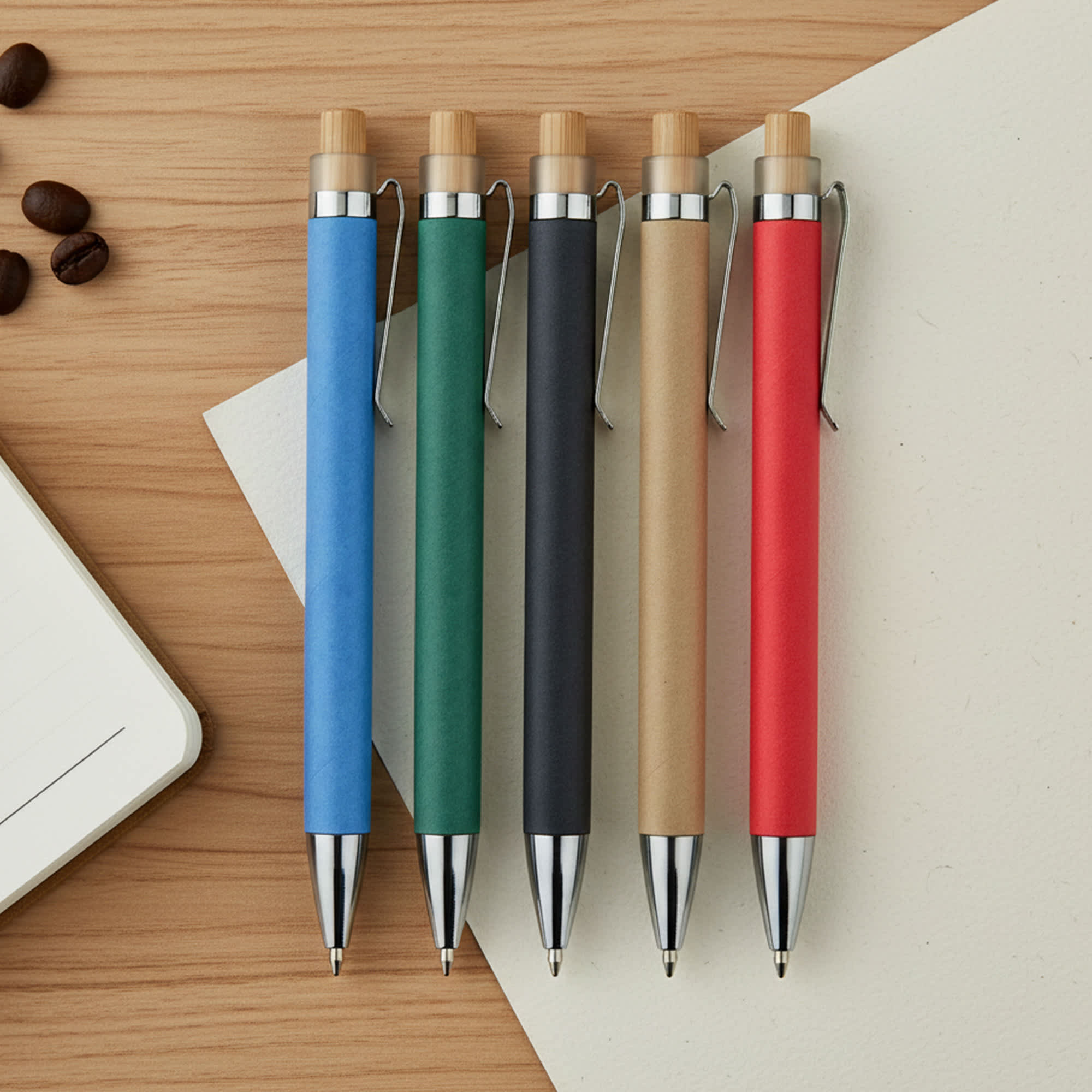 Five pens in various colours: blue, green, black, tan, and red, with wooden accents and silver clips, displayed on a wooden surface. Lanka Recycled Cardboard Pen - Image 1