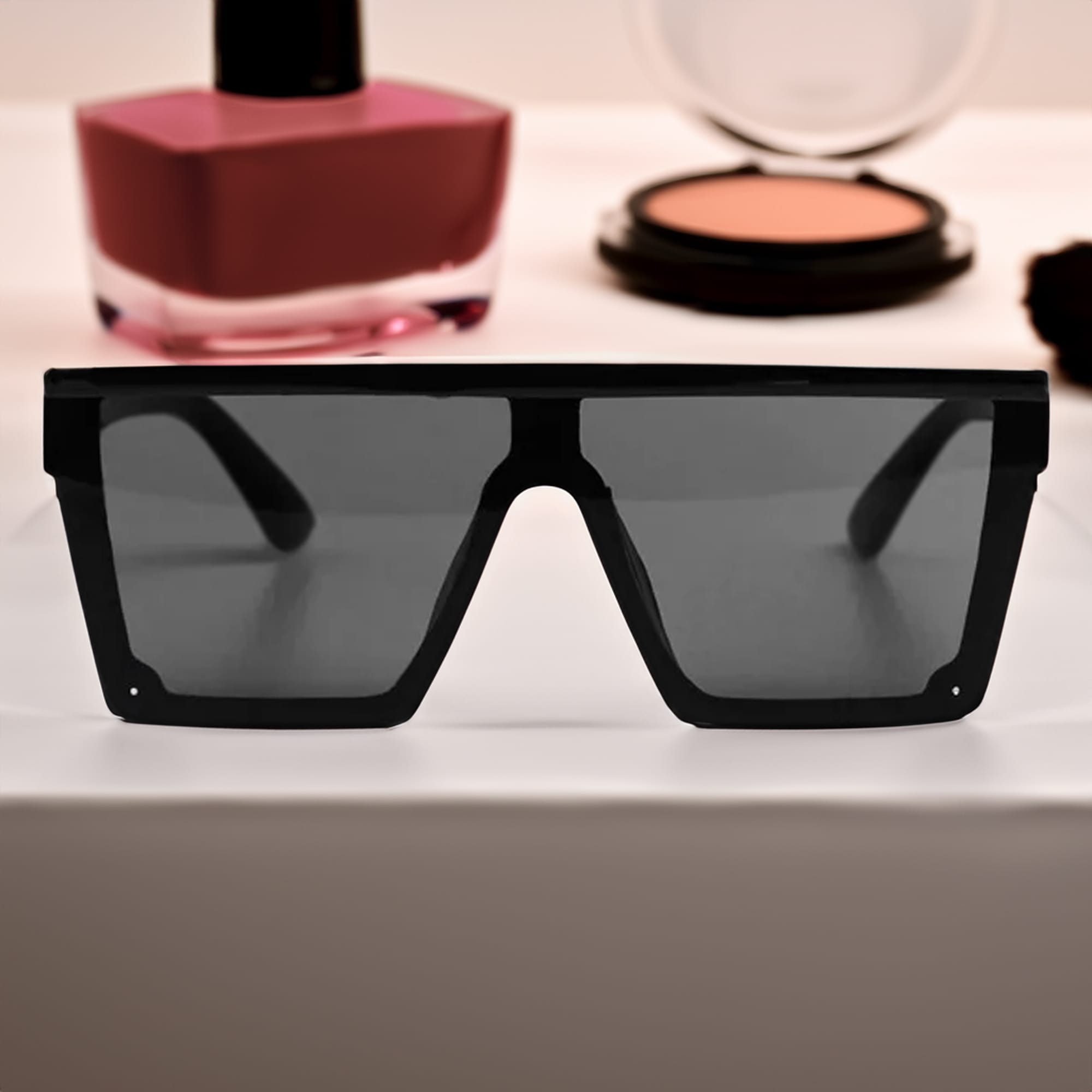 Black oversized sunglasses with dark lenses, displayed in front of cosmetics on a flat surface. Malibu Sunglasses - Image 1