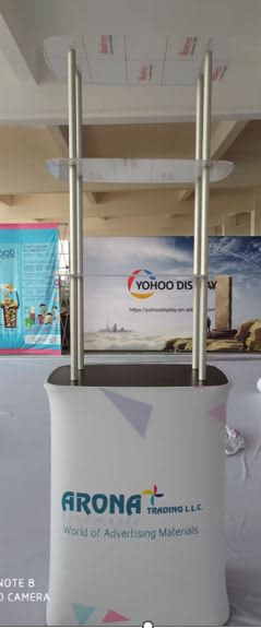 A promotional table with a stretch fabric covering, featuring two shelves and a sleek design in white and pastel colours. Stretch Fabric Promotion Table with Shelves - Image 1