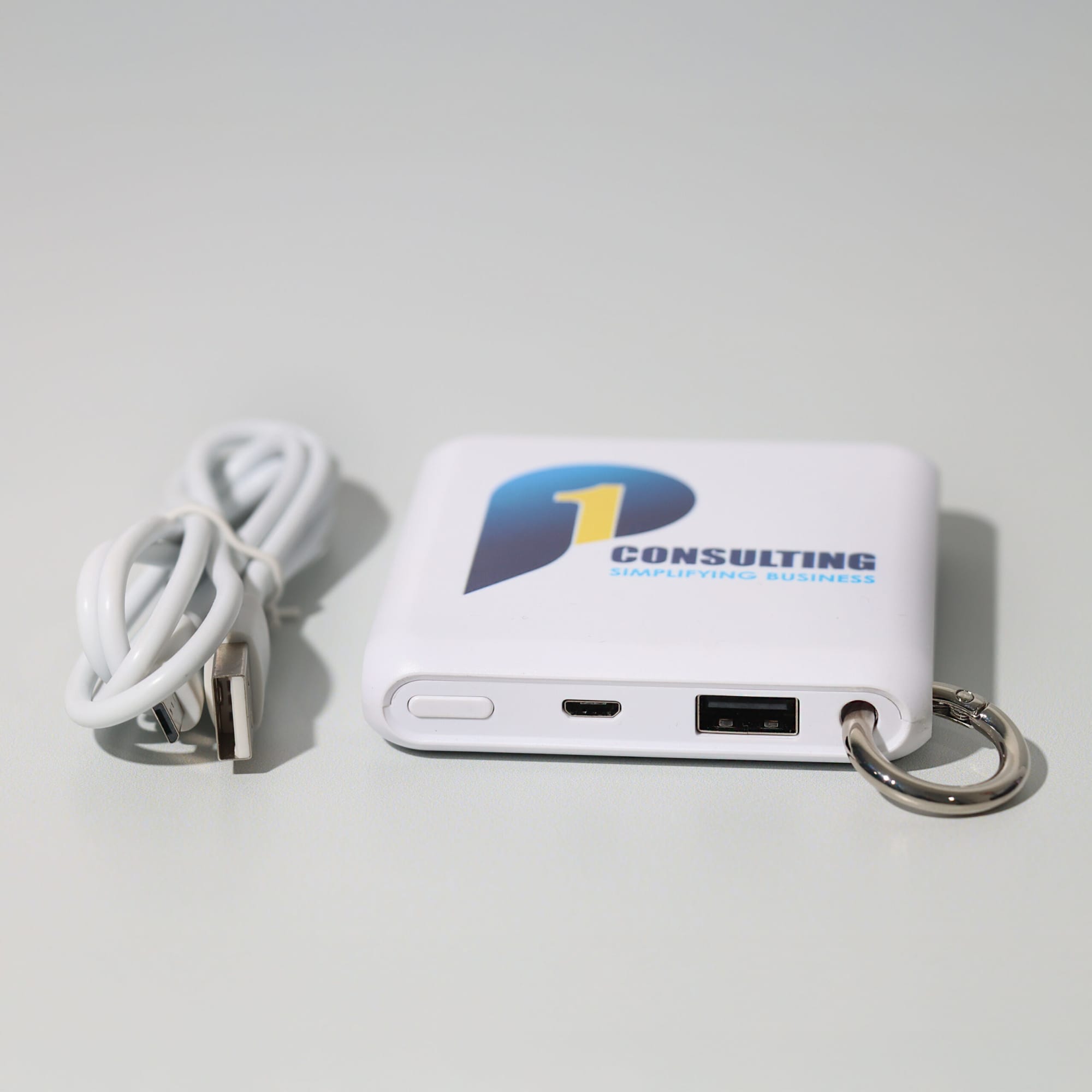 A white power bank with a logo, featuring USB ports and a keyring attachment, accompanied by a charging cable. Apollo Power Bank (5,000 mAh) - Image 1