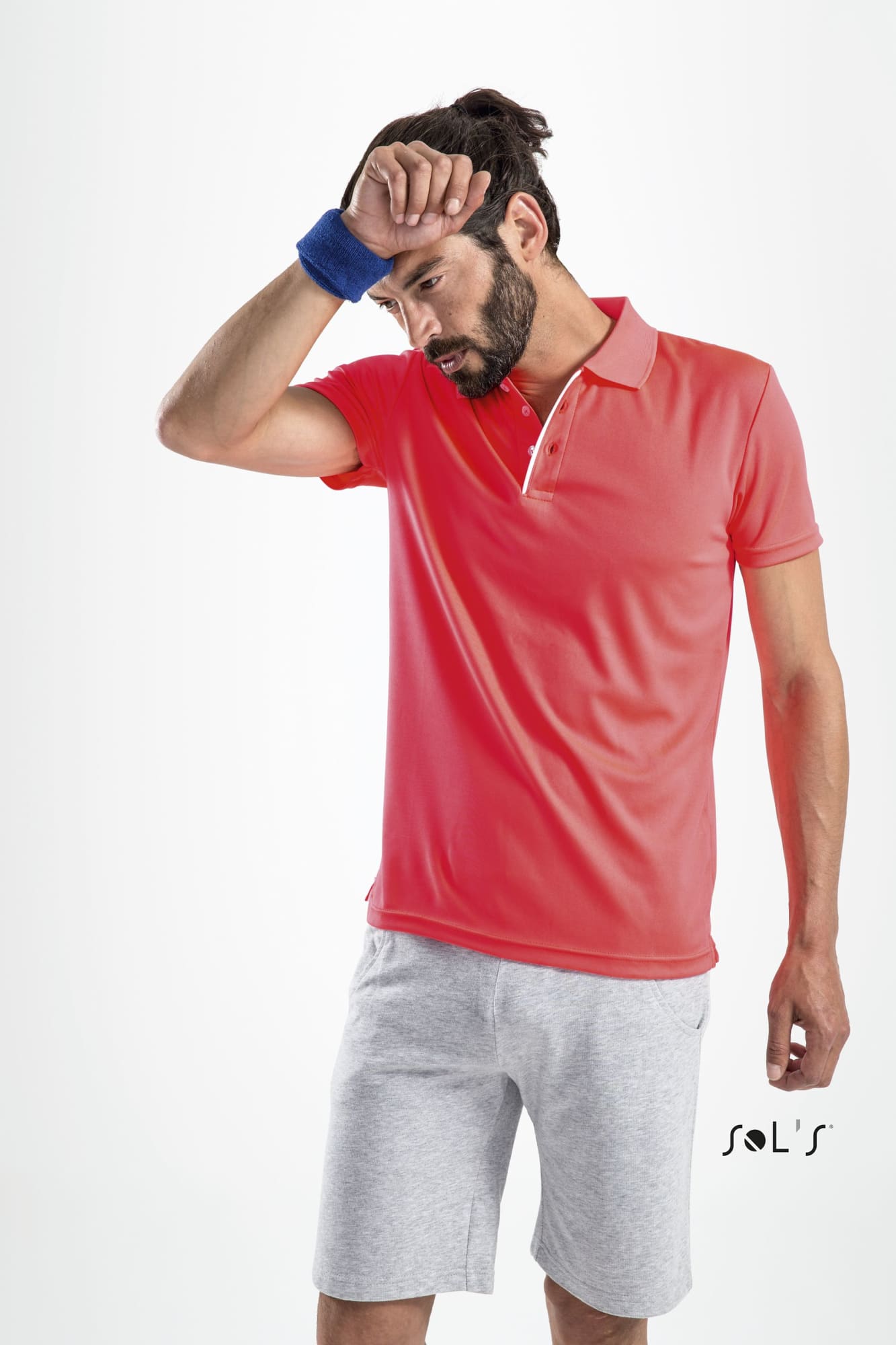 A man in a coral polo shirt and grey shorts wipes his forehead, featuring a small logo on the shirt. Polo shirt men's sports 100% polyester PERFORMER - Image 1