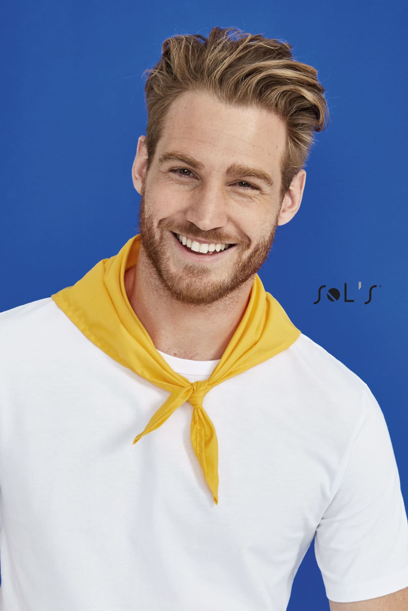 A triangular bandana in yellow, 62 x 62 x 87.5 cm, worn around the neck by a smiling man in a white t-shirt. BANDANA triangular shape 62 x 62 x 87.5cm - Image 1
