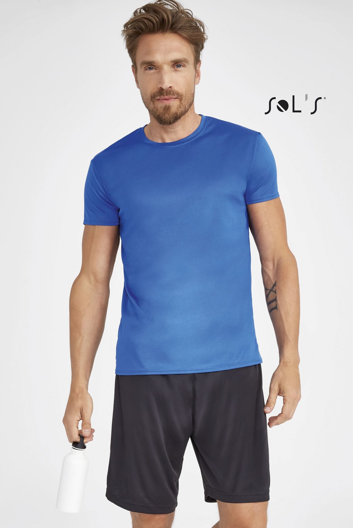 A man in a blue short-sleeve T-shirt and black shorts, holding a drink bottle. The shirt features a logo. T shirt UNISEX 100% polyester SPRINT UNISEX - Image 1