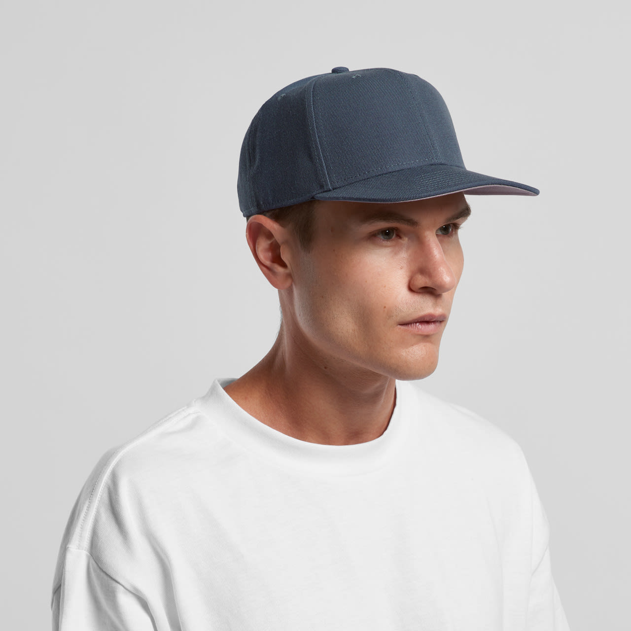 A blue cap with a structured design and a logo, worn by a model in a white t-shirt. Stock Cap - Image 1