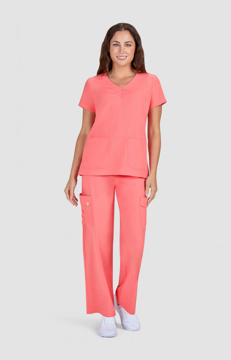 A pair of coral scrubs featuring a short-sleeve top and long pants, with pockets, worn by a model. Enik Top - Image 1