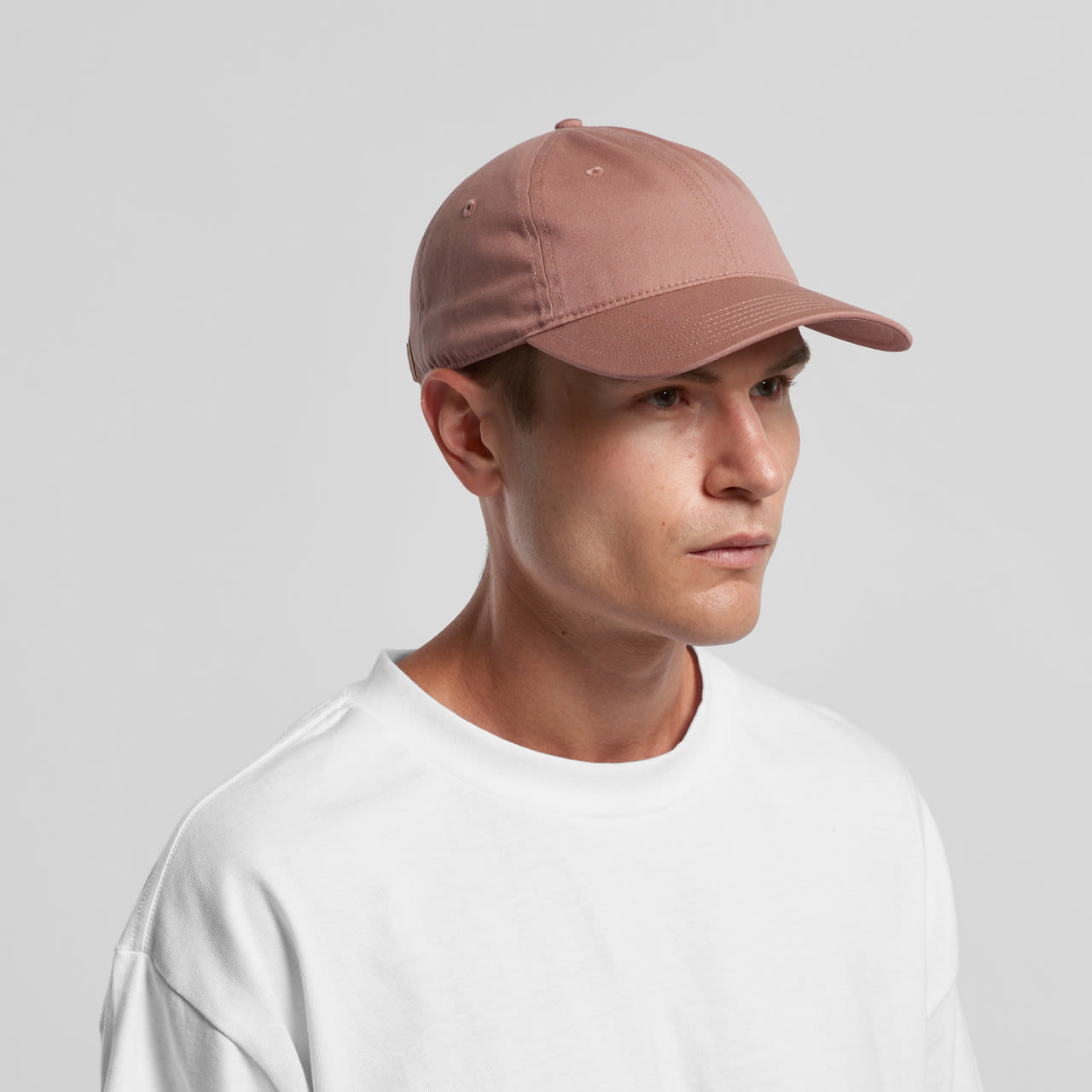 A pink cap with a curved brim and a logo, worn by a model in a white sweatshirt. Access Cap - Image 1